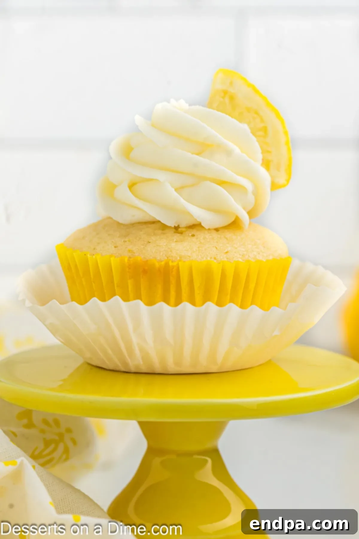 A perfectly frosted lemon cupcake with a fresh lemon slice on top, sitting on a white background.