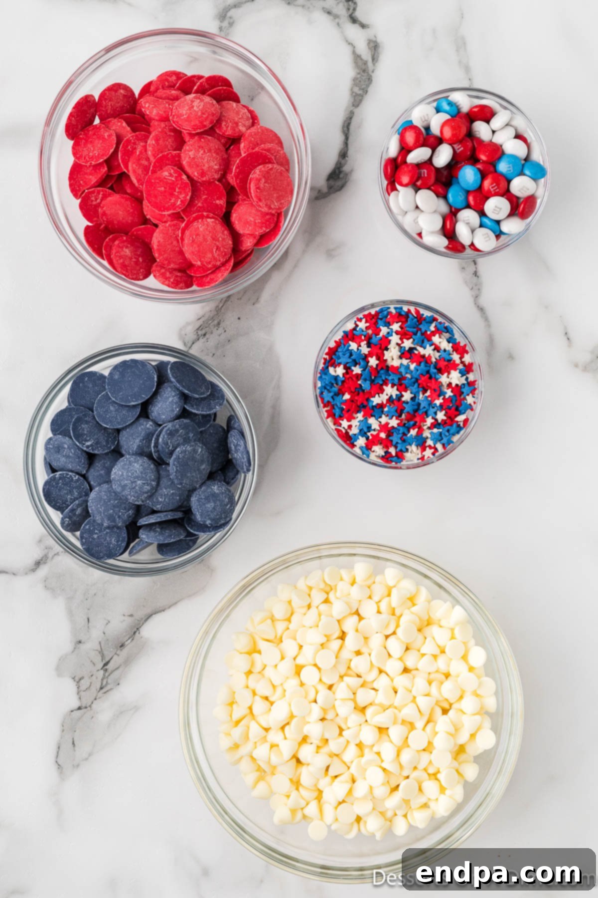 Ingredients for red white and blue bark recipe - red white and blue m&ms, white chocolate chips, patriotic sprinkles, blue and red candy melts in bowls.