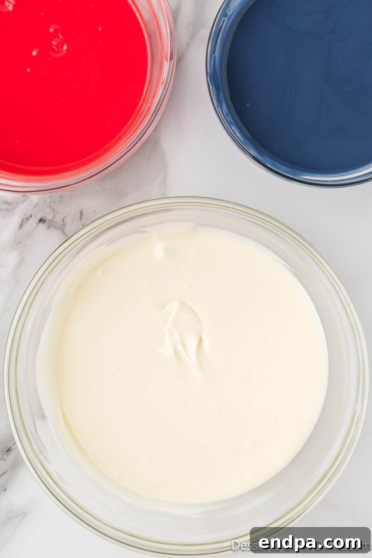 Three separate bowls: one with melted white chocolate, one with melted red candy melts, and one with melted blue candy melts.