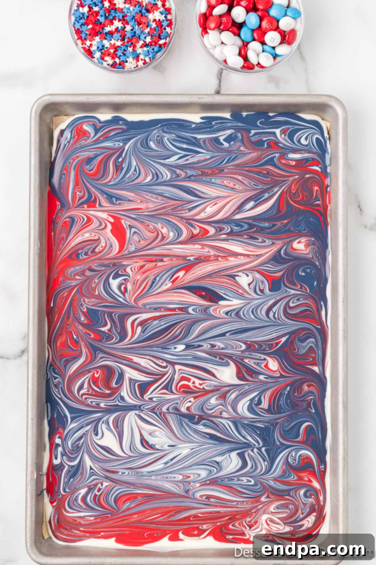 Swirled red, white, and blue melted chocolate on a baking sheet, creating a marbled effect.