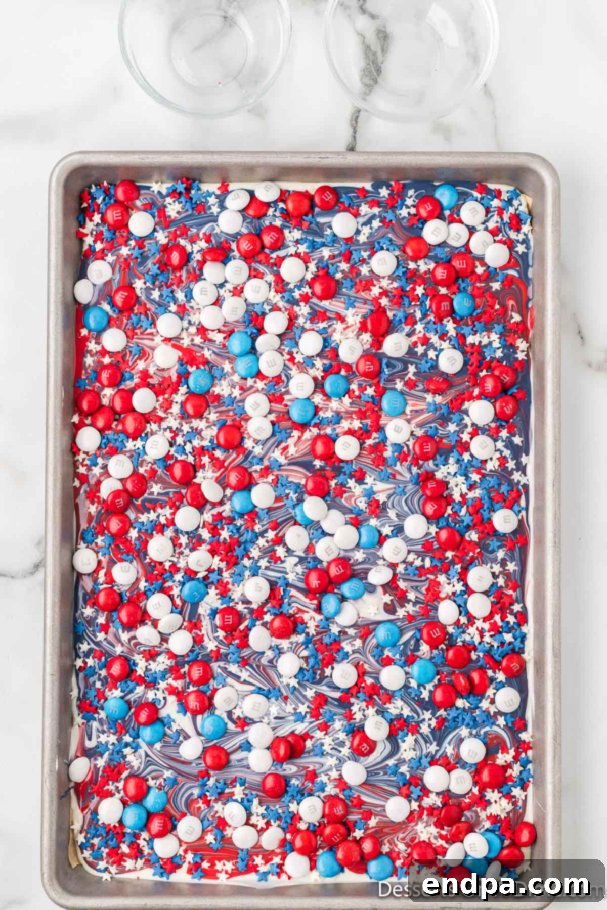 Red, white, and blue M&M's and star sprinkles on top of swirled melted chocolate, ready to chill.