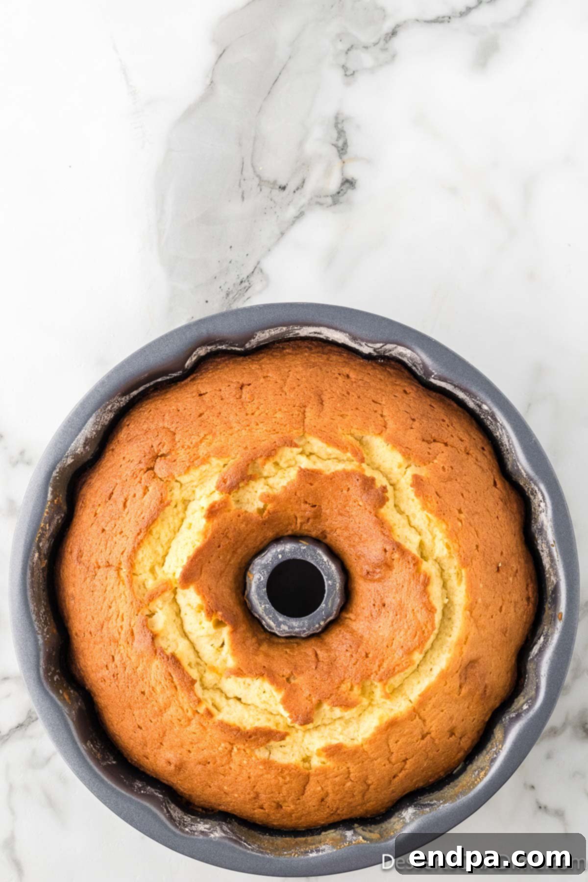 Dreamy Cream Cheese Pound Cake 14 A freshly baked pound cake, golden brown and still in its bundt pan, rests on a cooling rack, allowing it to set before being inverted.