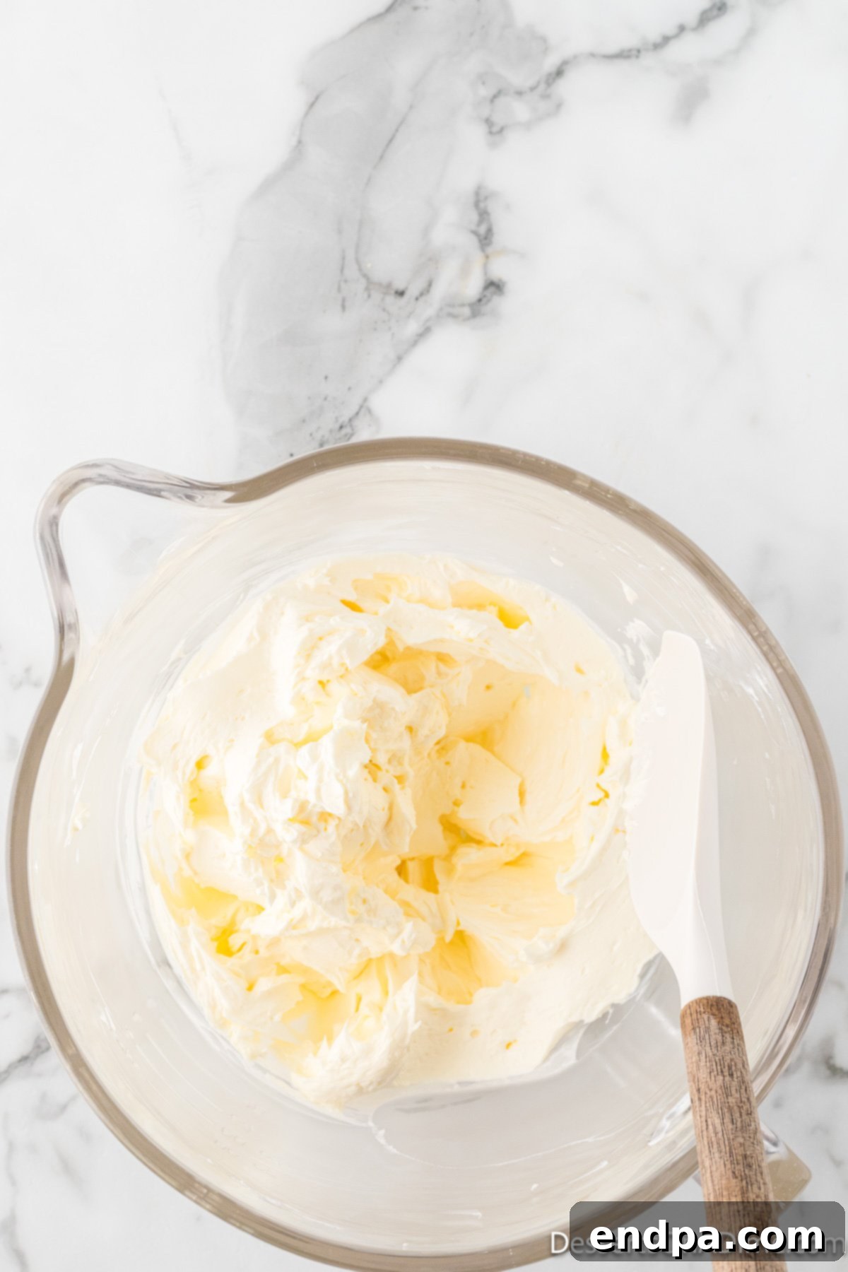 Dreamy Cream Cheese Pound Cake 6 A spatula carefully scrapes down the sides of the mixing bowl, ensuring all butter and cream cheese are incorporated evenly into the pound cake batter.