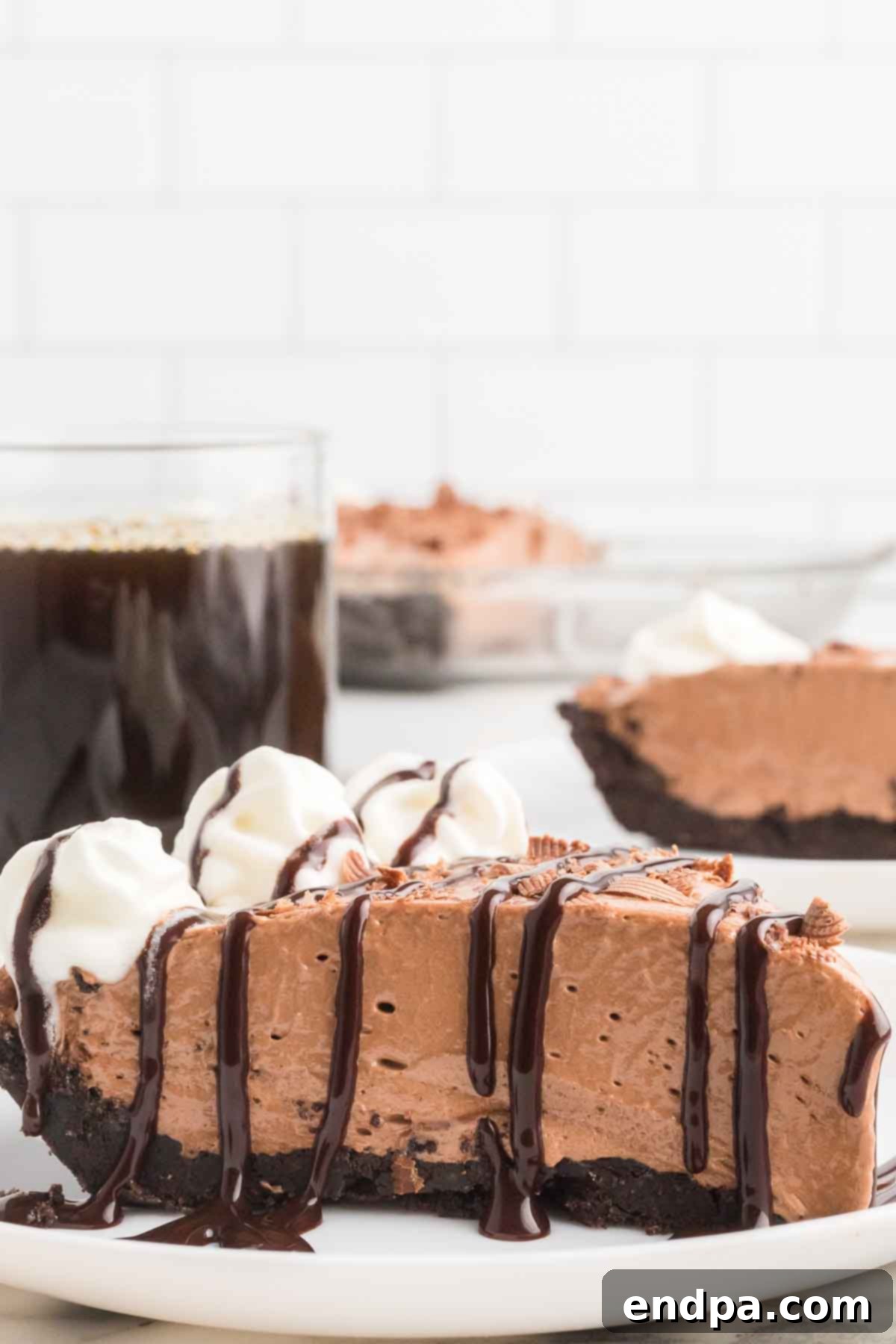 A perfectly sliced no-bake Nutella Pie on a white plate, showcasing its creamy filling and dark Oreo crust, topped with whipped cream and chocolate shavings.