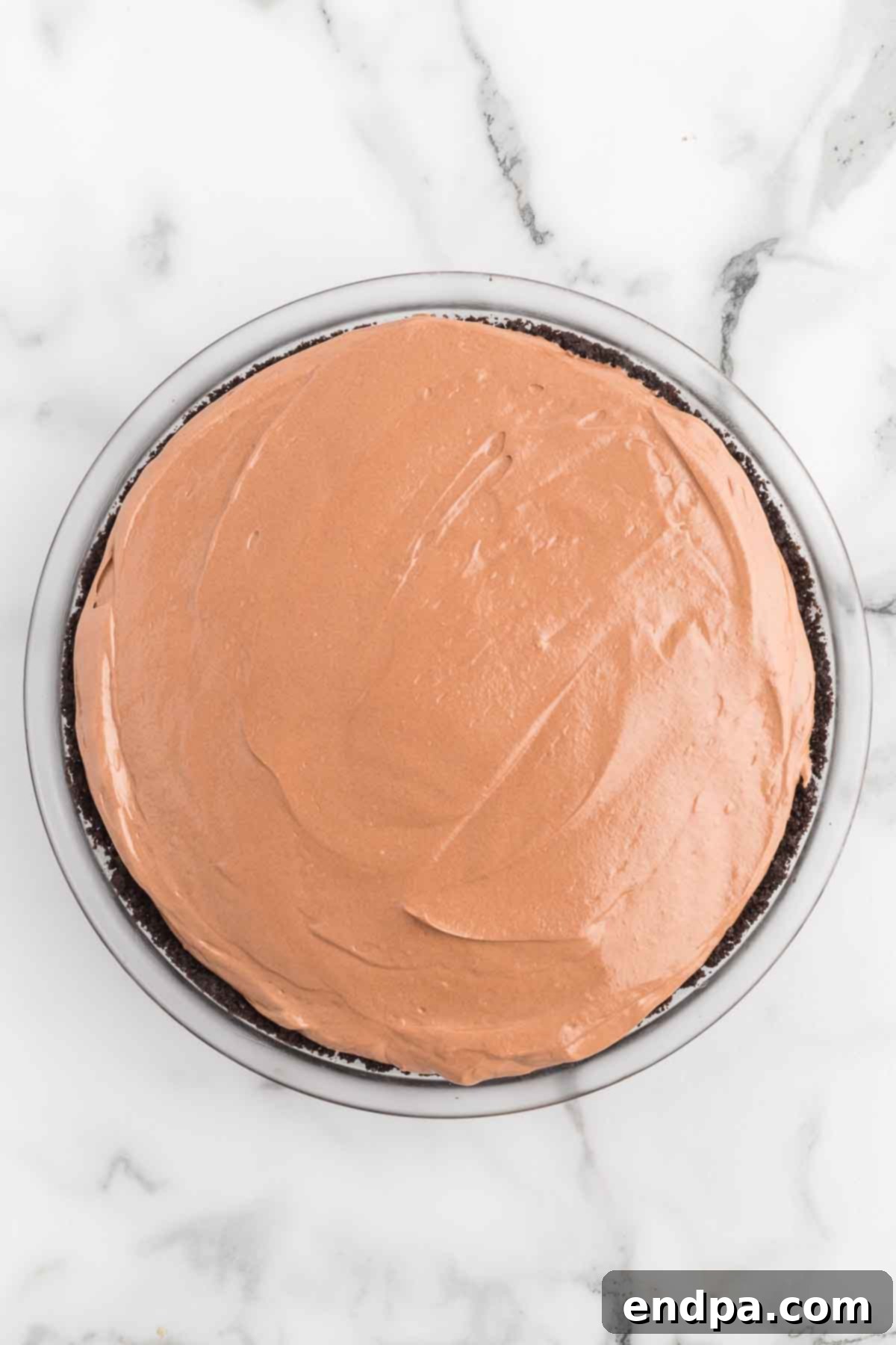The smooth Nutella pie filling being poured and spread into the chilled Oreo crust.