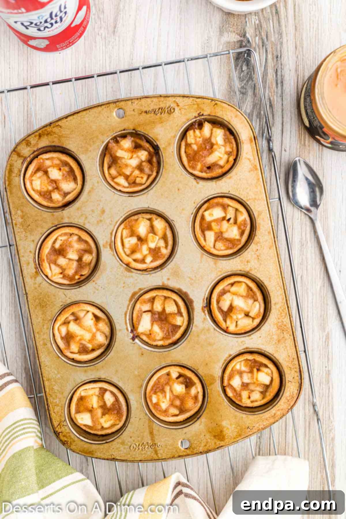 A mini muffin pan filled with freshly baked apple pie bites cooling on a wire rack.