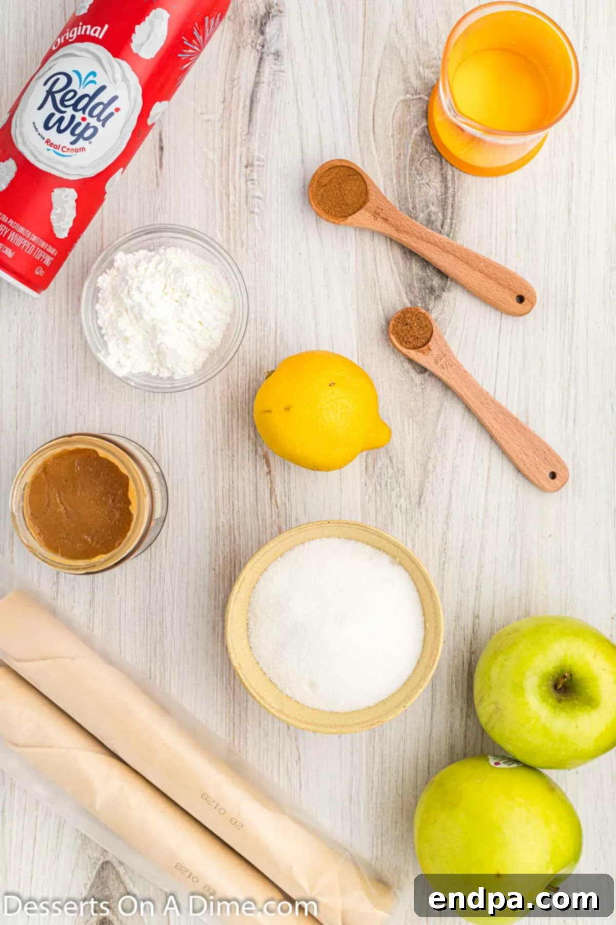 A flat lay photograph displaying all the fresh ingredients needed to make Mini Apple Pie Bites, including apples, spices, sugar, and pie crust.