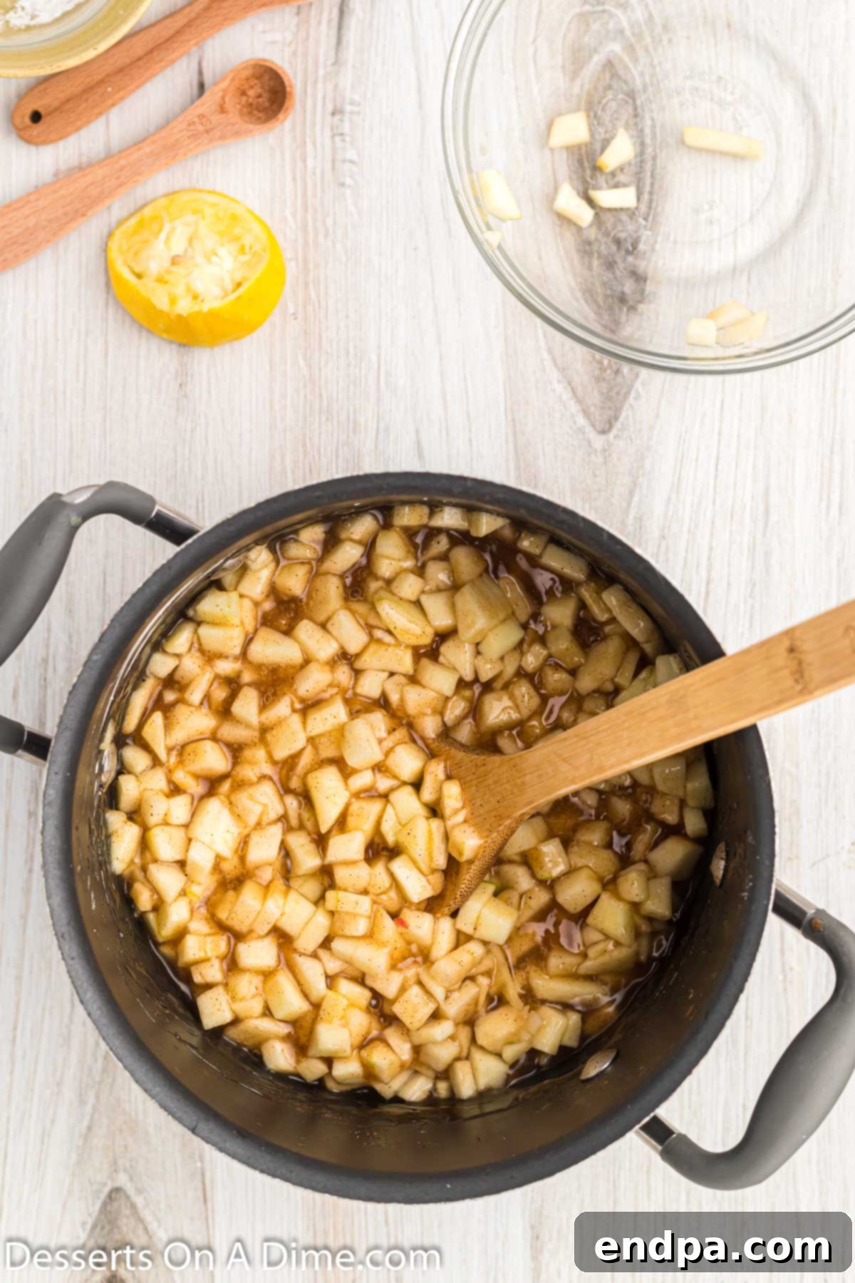 Diced fresh apples being added to the thickened cinnamon-sugar sauce in the saucepan.