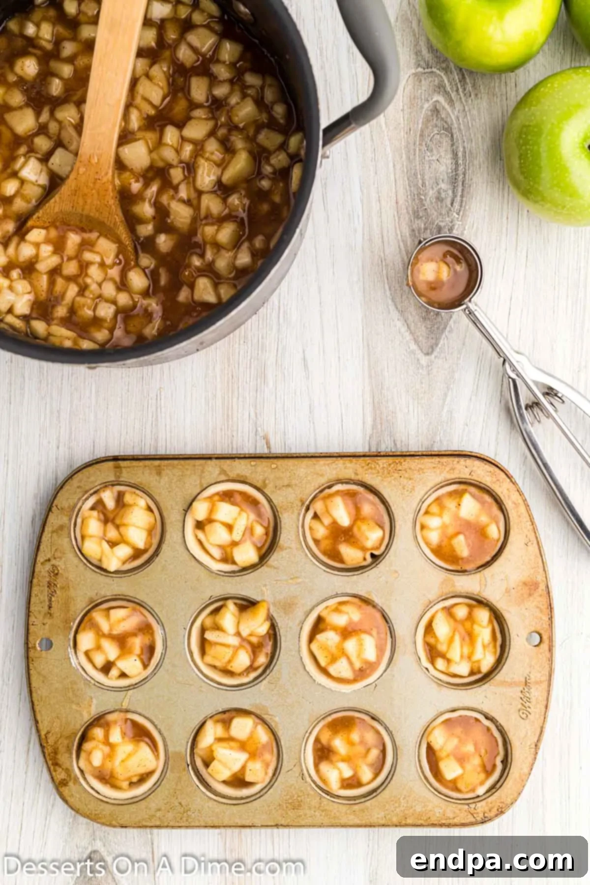The mini muffin tin with individual pie crusts filled with apple pie filling, ready for baking.