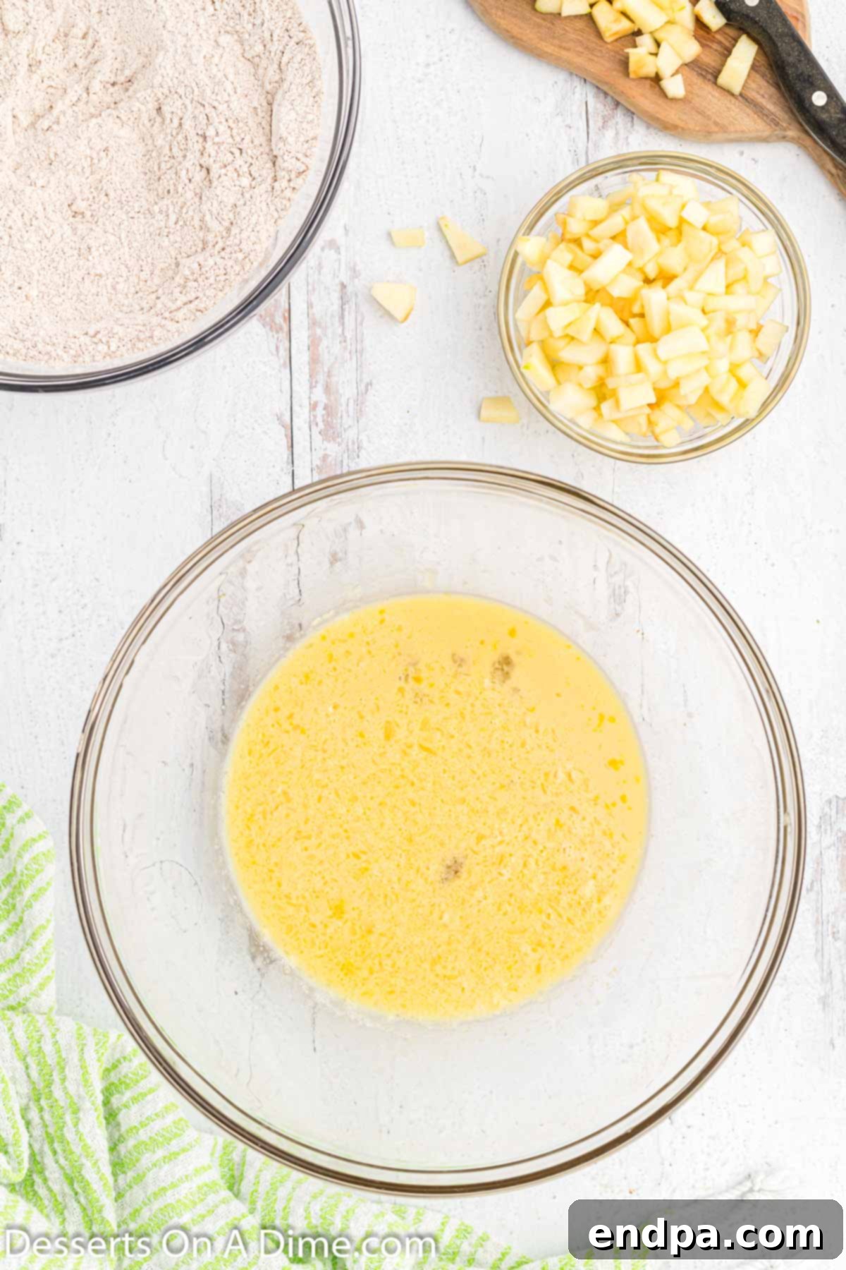 Golden Crisp Apple Fritters 5 A separate mixing bowl holding the combined wet ingredients for apple fritters: milk, eggs, cooled melted butter, and vanilla extract, stirred to a smooth consistency.