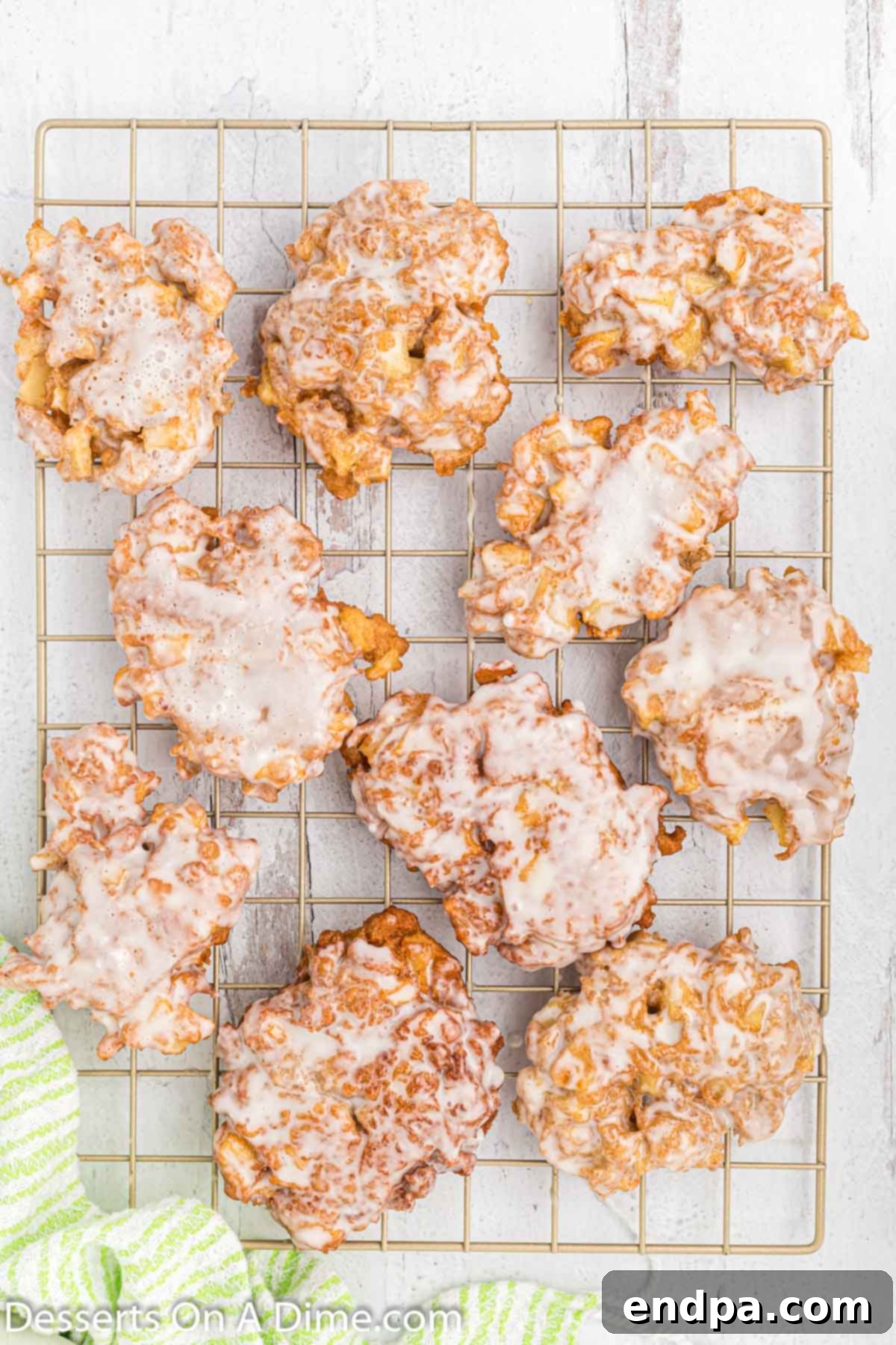 Golden Crisp Apple Fritters 7 Freshly fried apple fritters resting on a wire cooling rack, allowing excess oil to drain and preparing them for the glaze, with a light golden-brown color.