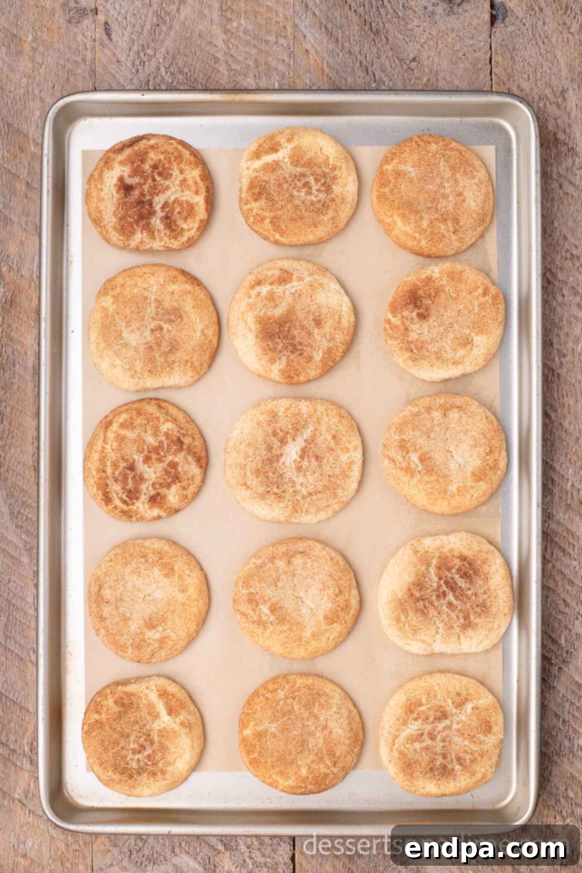 Simple Snickerdoodle Perfection 7 Unbaked Snickerdoodle cookie dough balls, coated in cinnamon sugar, arranged on a baking sheet.