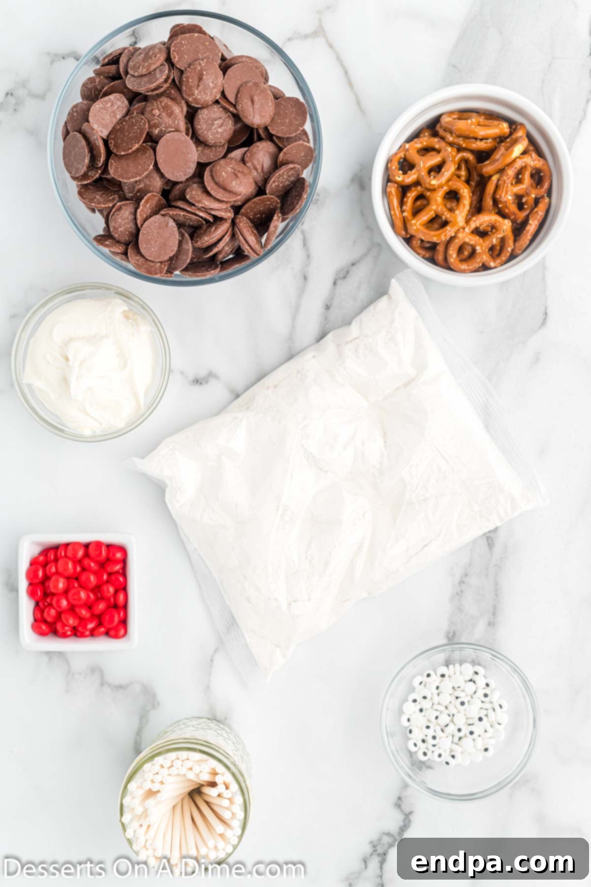 A flat lay of ingredients for Reindeer Cake Pops including vanilla cake mix, vanilla frosting, chocolate candy melts, candy eyes, red hots candy, and small pretzels.