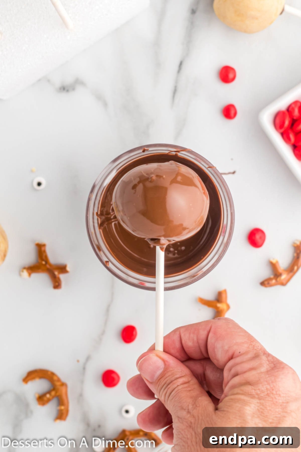 A Reindeer Cake Pop freshly dipped in smooth chocolate coating, with excess chocolate dripping off.