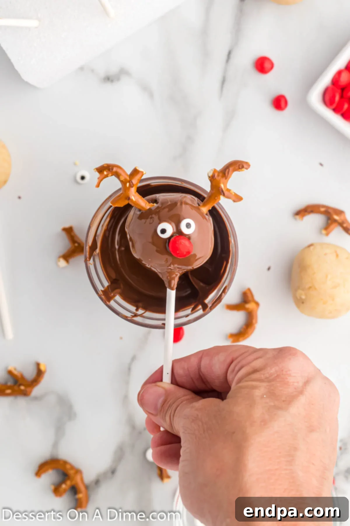 Reindeer Cake Pops decorated with pretzel antlers, candy eyes, and a red hot nose, ready to dry.