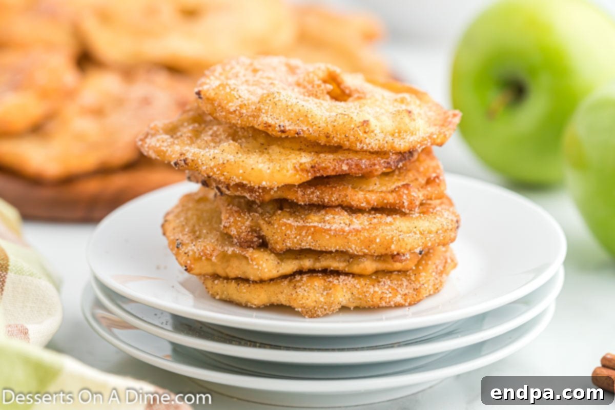 Crispy, golden deep fried apples stacked together on a white plate, dusted with cinnamon sugar.