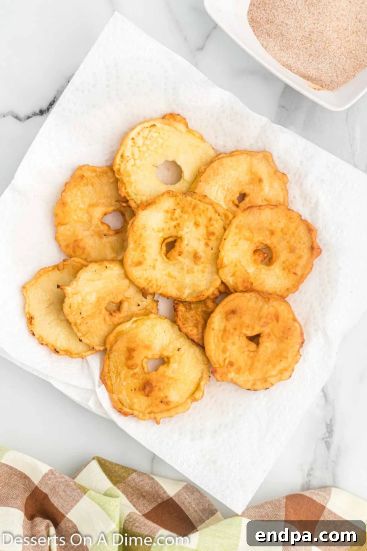 Freshly fried apple slices cooling on a plate lined with paper towels to absorb excess oil.