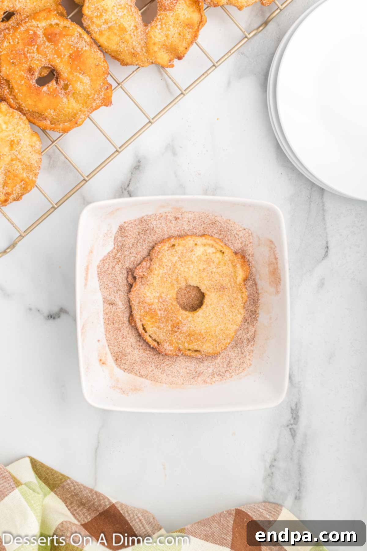 Warm fried apple slices being dipped into a bowl of cinnamon sugar mixture.