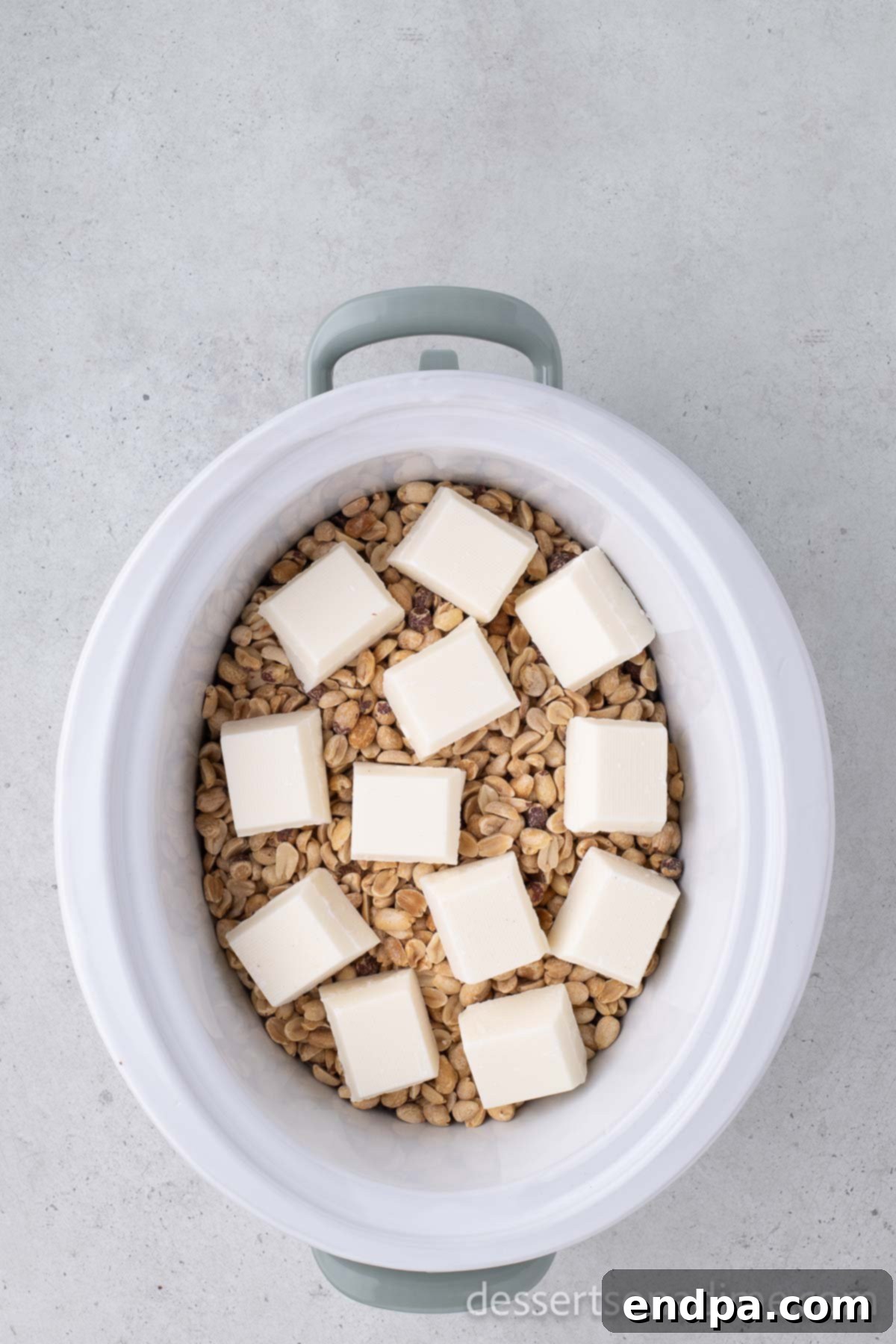 White almond bark broken into squares on top of the mixture in a crock pot.