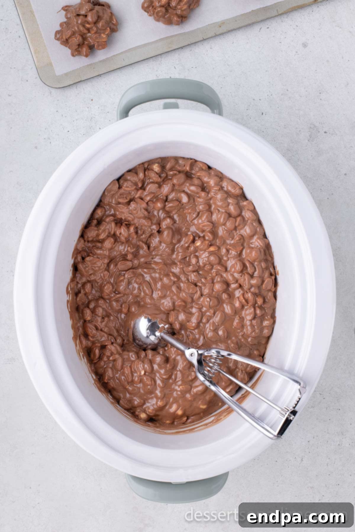 A crock pot with the melted mixture and a cookie scoop inside, ready to scoop.