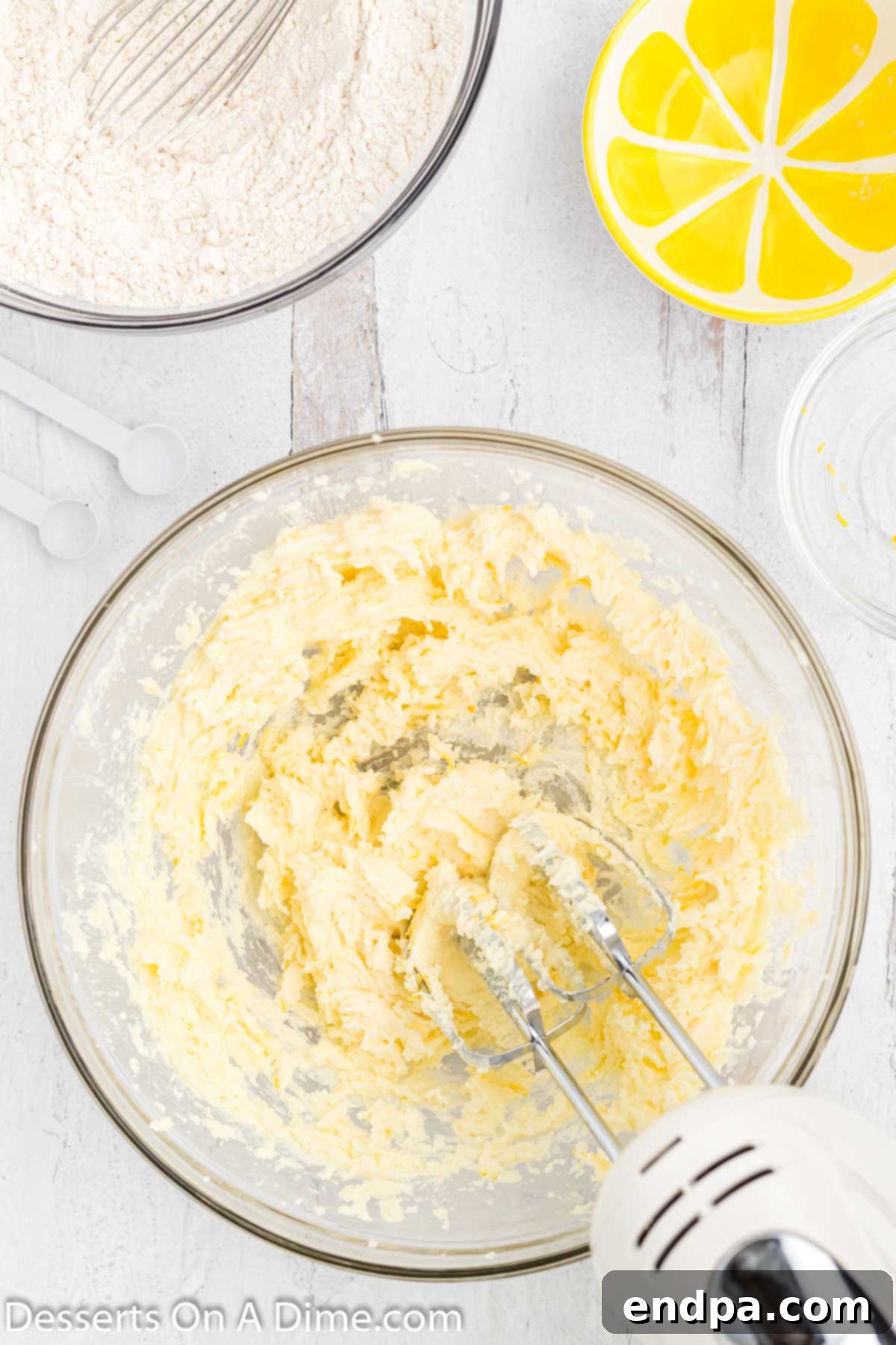 Softened butter, granulated sugar, and lemon zest being creamed together in a large mixing bowl with a hand mixer.