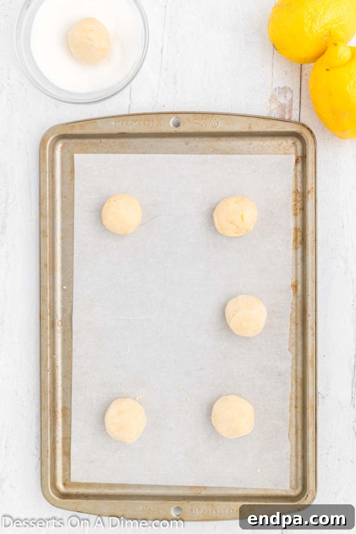 Portion-sized cookie dough balls rolled in granulated sugar and placed on a parchment-lined baking sheet.