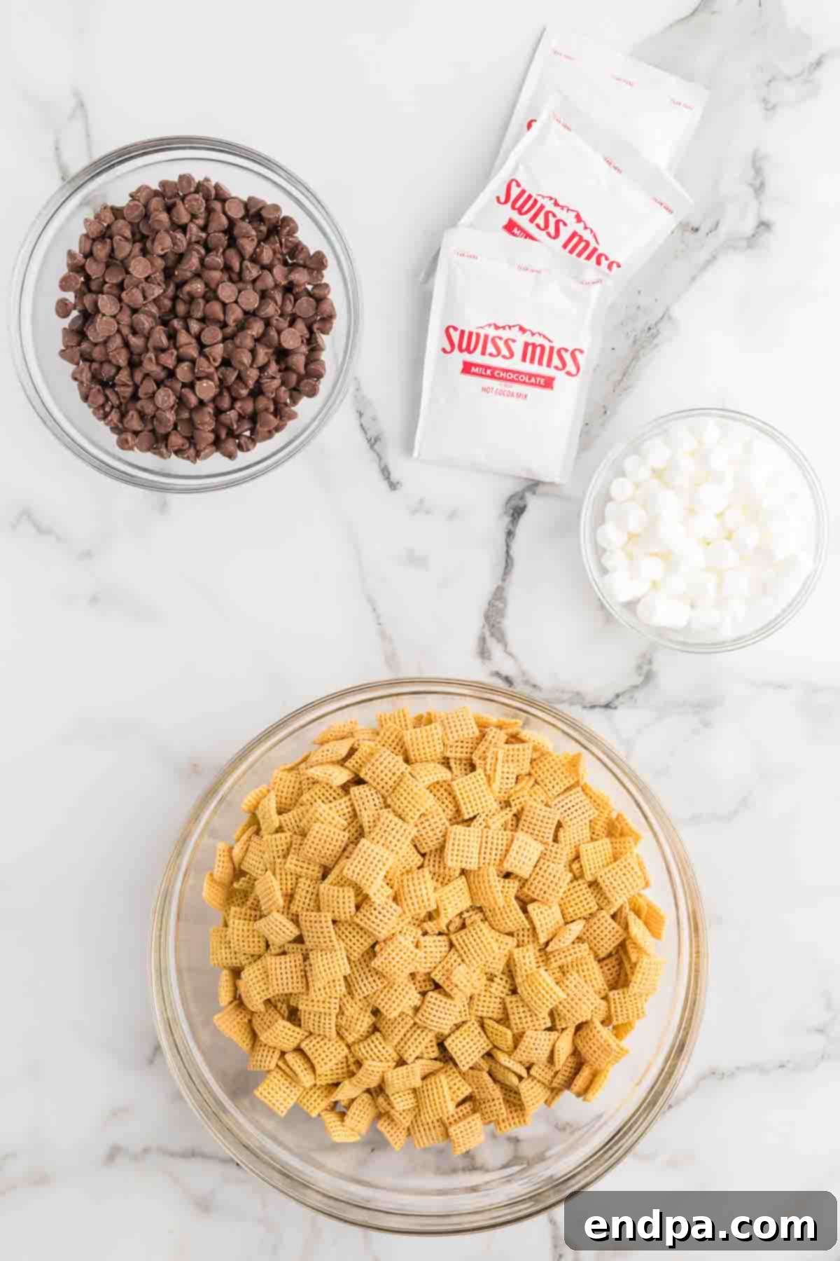 Decadent Hot Chocolate Puppy Chow 3 Ingredients for hot chocolate puppy chow laid out: milk chocolate chips, Chex cereal, hot chocolate mix, mini marshmallows.