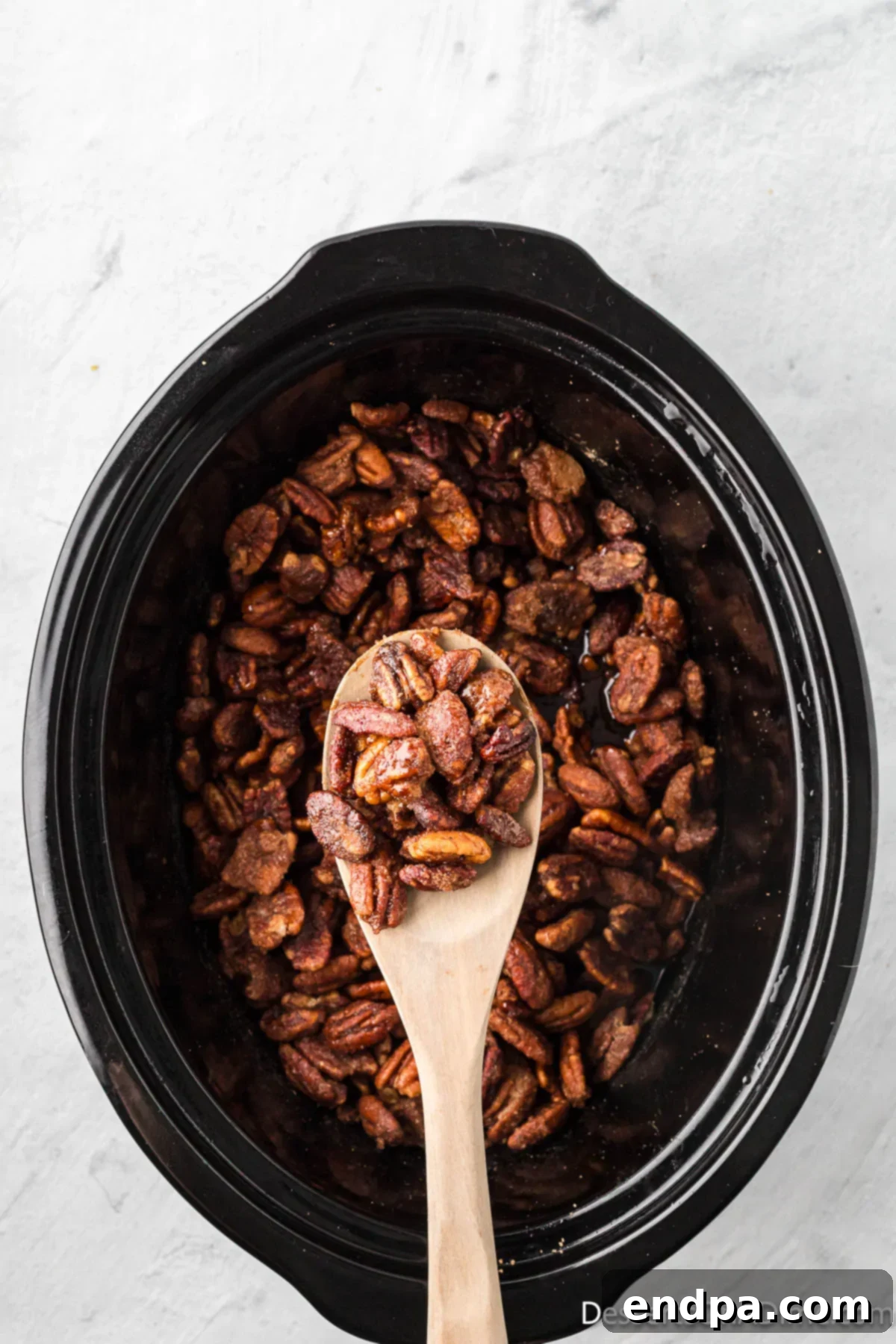 Pecans in crock pot with a spoon. 