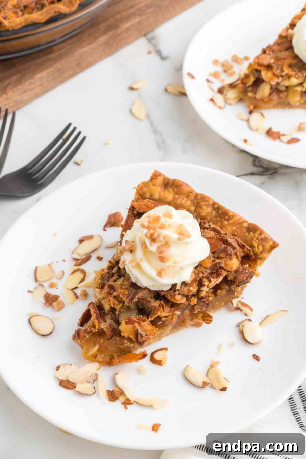 A glorious slice of Toffee Almond Pie, generously topped with a swirl of fresh whipped cream and a sprinkle of almond slivers, ready to be devoured.