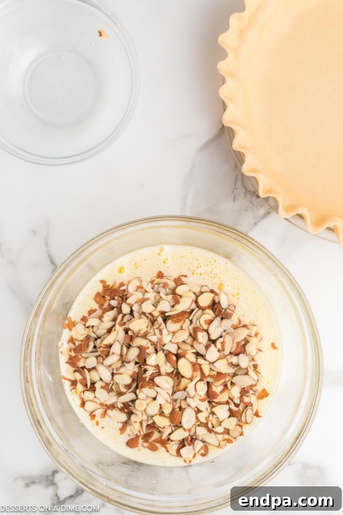 Perfectly coated sliced almonds mixed into the glossy, amber pie batter in a bowl, promising a delightful crunch.