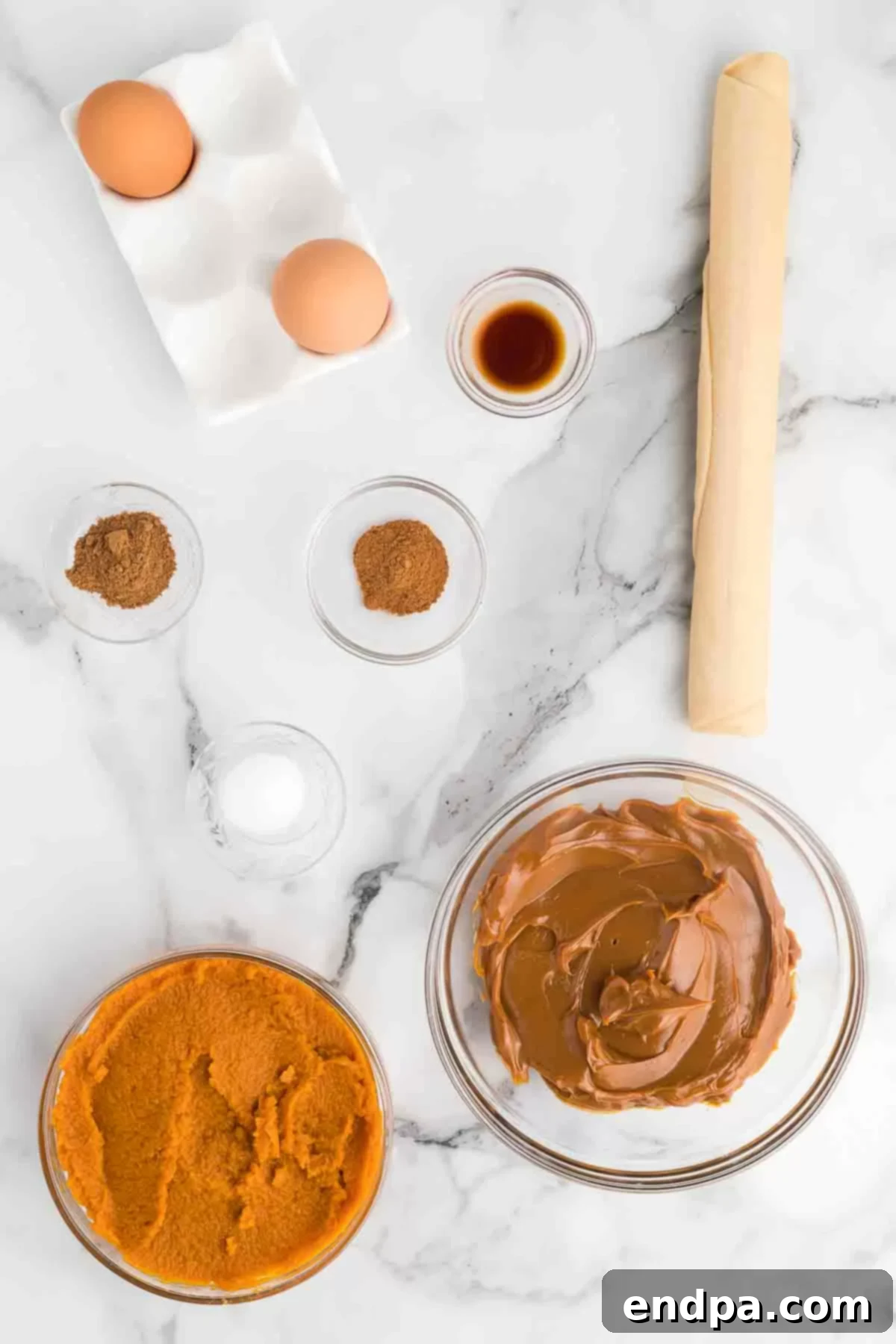 Luscious Dulce De Leche Pumpkin Pie 3 A collection of ingredients laid out: an unbaked pie crust, a can of pumpkin puree, a jar of dulce de leche, a bottle of vanilla extract, a small bowl of salt, pumpkin pie spice, cinnamon sticks, and fresh eggs.