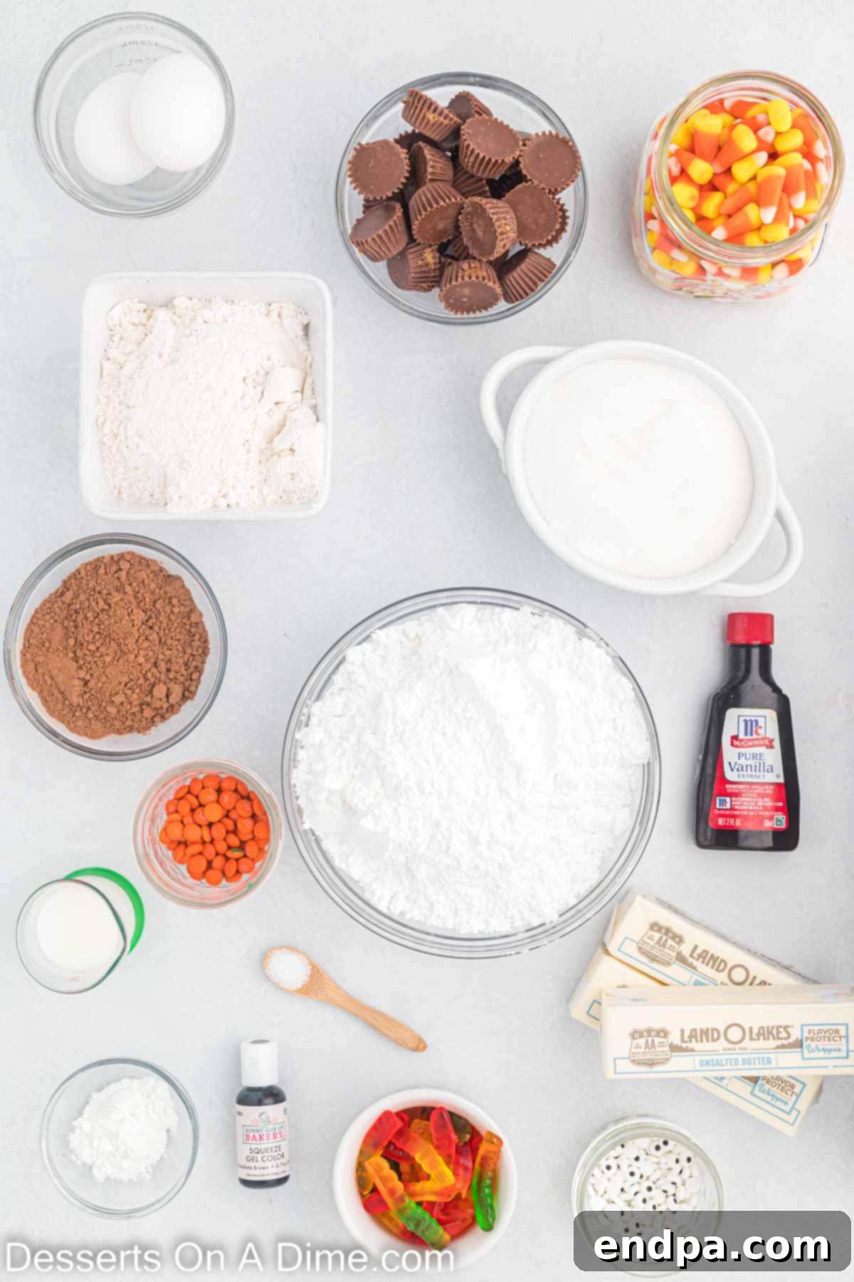 A collection of ingredients for Thanksgiving sugar cookies, including flour, butter, egg, egg yolk, vanilla extract, powdered sugar, cocoa powder, milk, mini Reese's cups, candy eyes, gummy worms, candy corn, and orange mini M&M's.