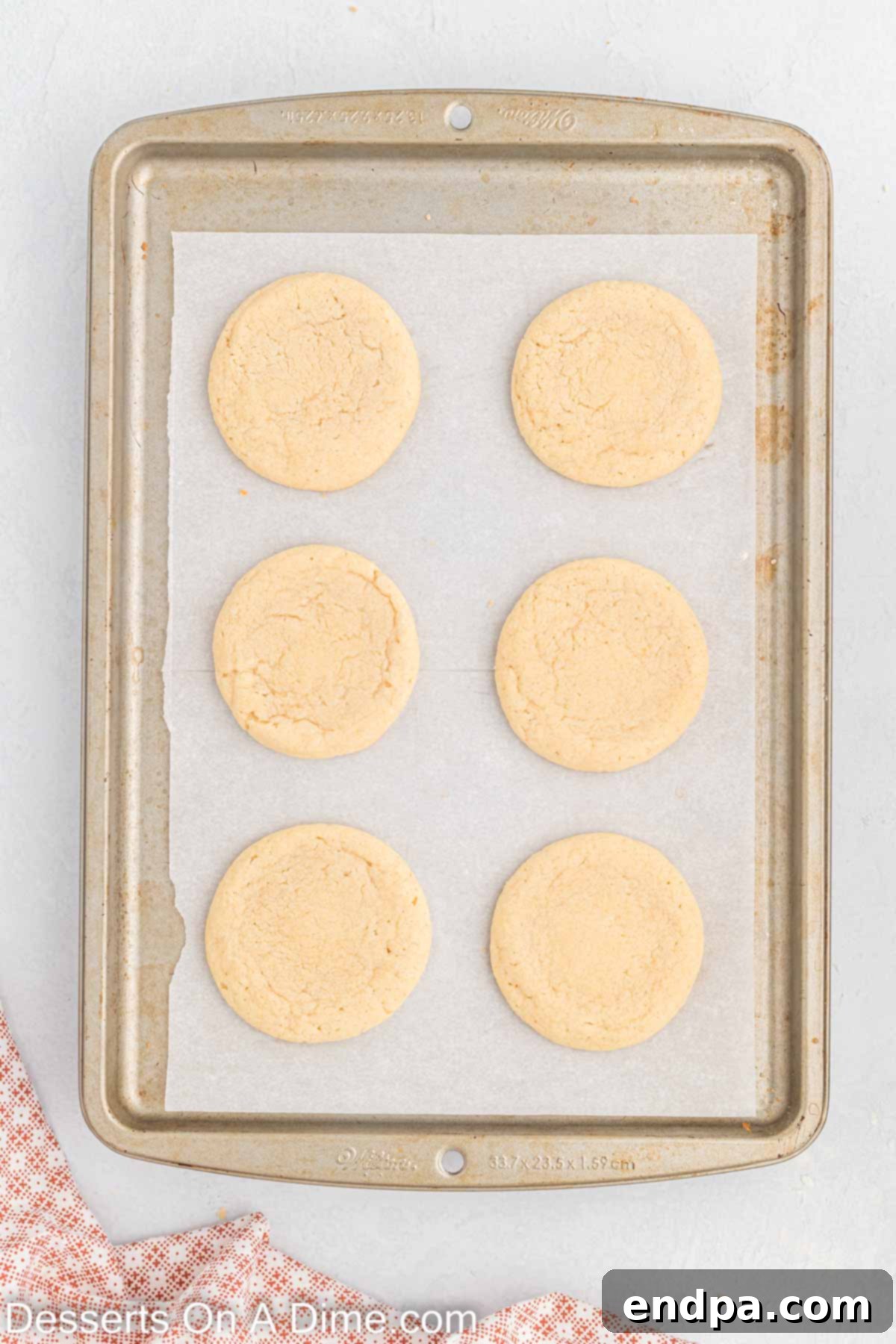 Freshly baked sugar cookies cooling on a baking sheet.