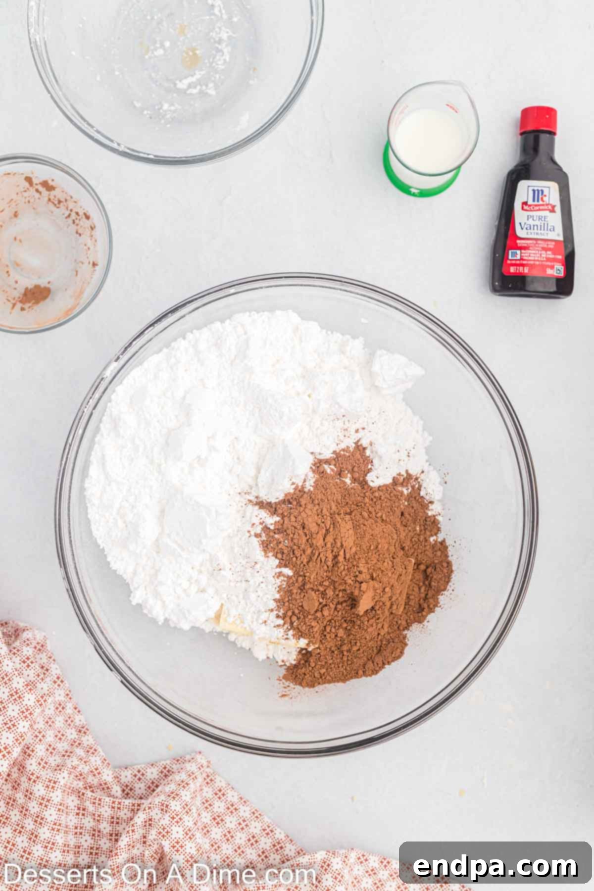 Dry ingredients for chocolate frosting, including powdered sugar and cocoa powder, in a mixing bowl.
