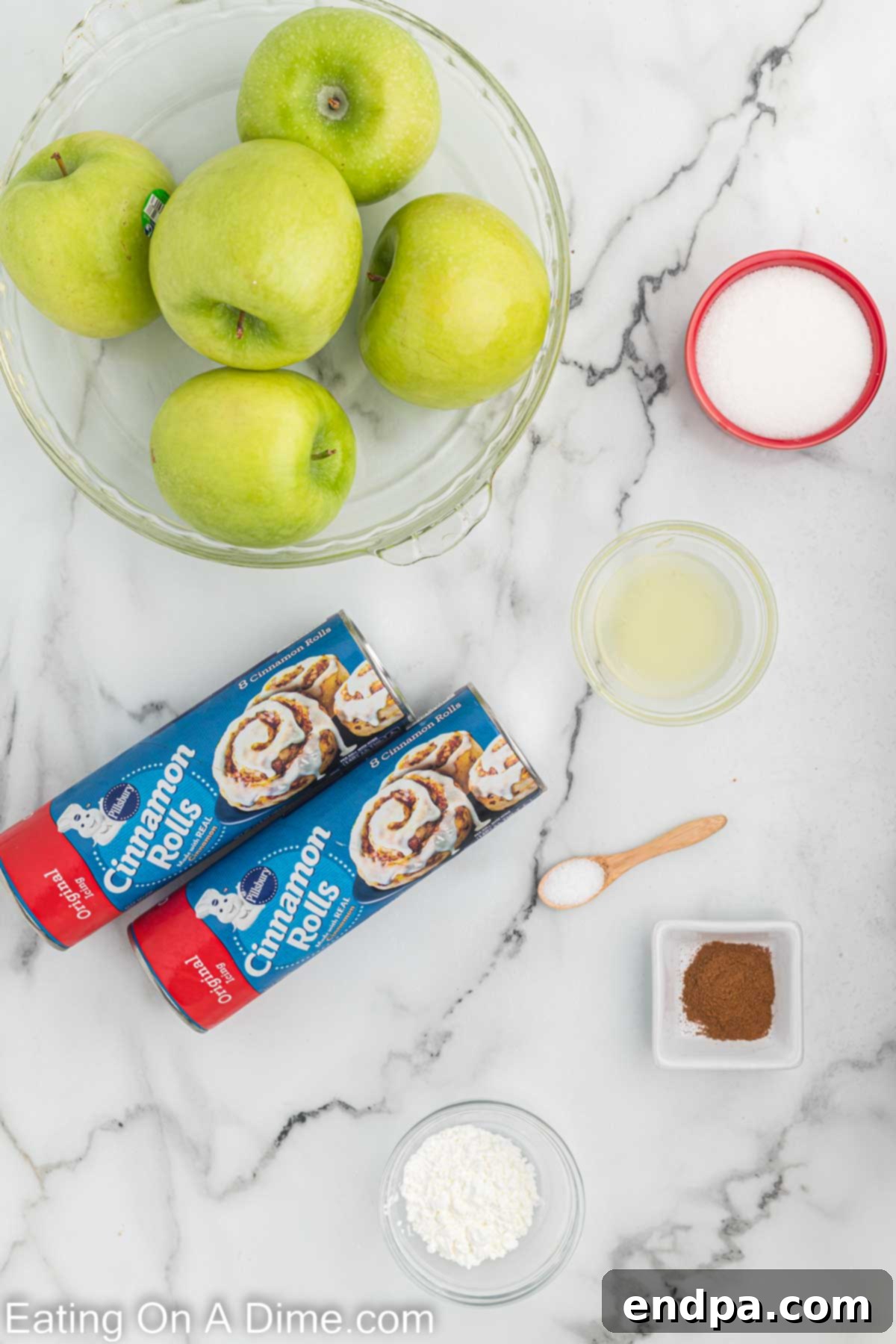 Key ingredients for Cinnamon Roll Apple Pie laid out: two cans of cinnamon rolls, fresh Granny Smith apples, a lemon, and a jar of ground cinnamon.