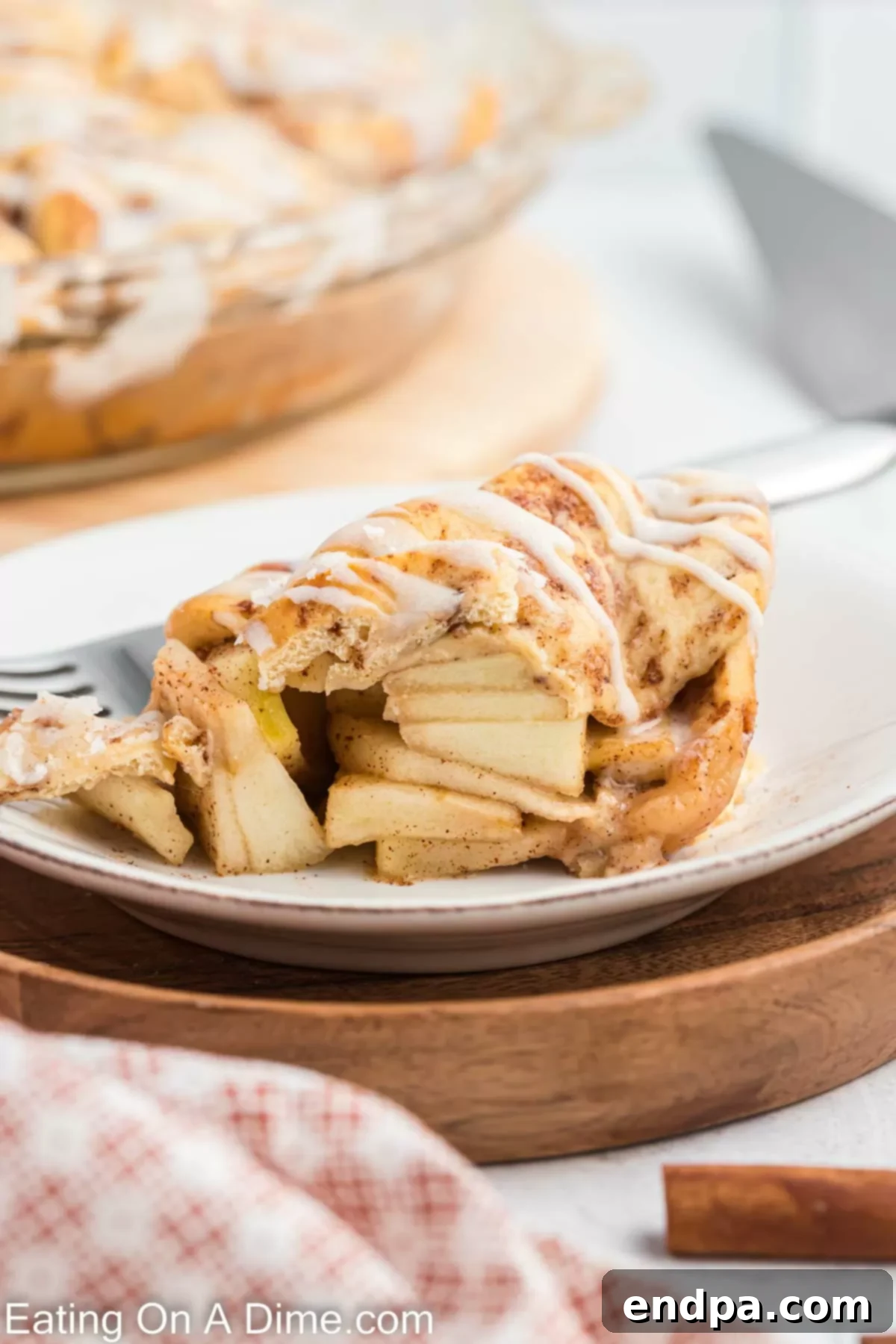 A slice of Cinnamon Roll Apple Pie on a plate, adorned with a scoop of vanilla ice cream and a caramel drizzle, ready to be enjoyed.