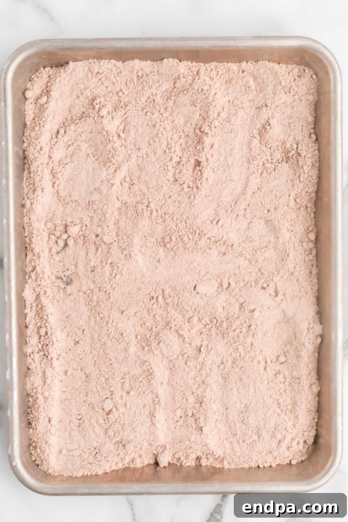 Red velvet cake mix spread evenly on a baking sheet, ready for heat treatment.