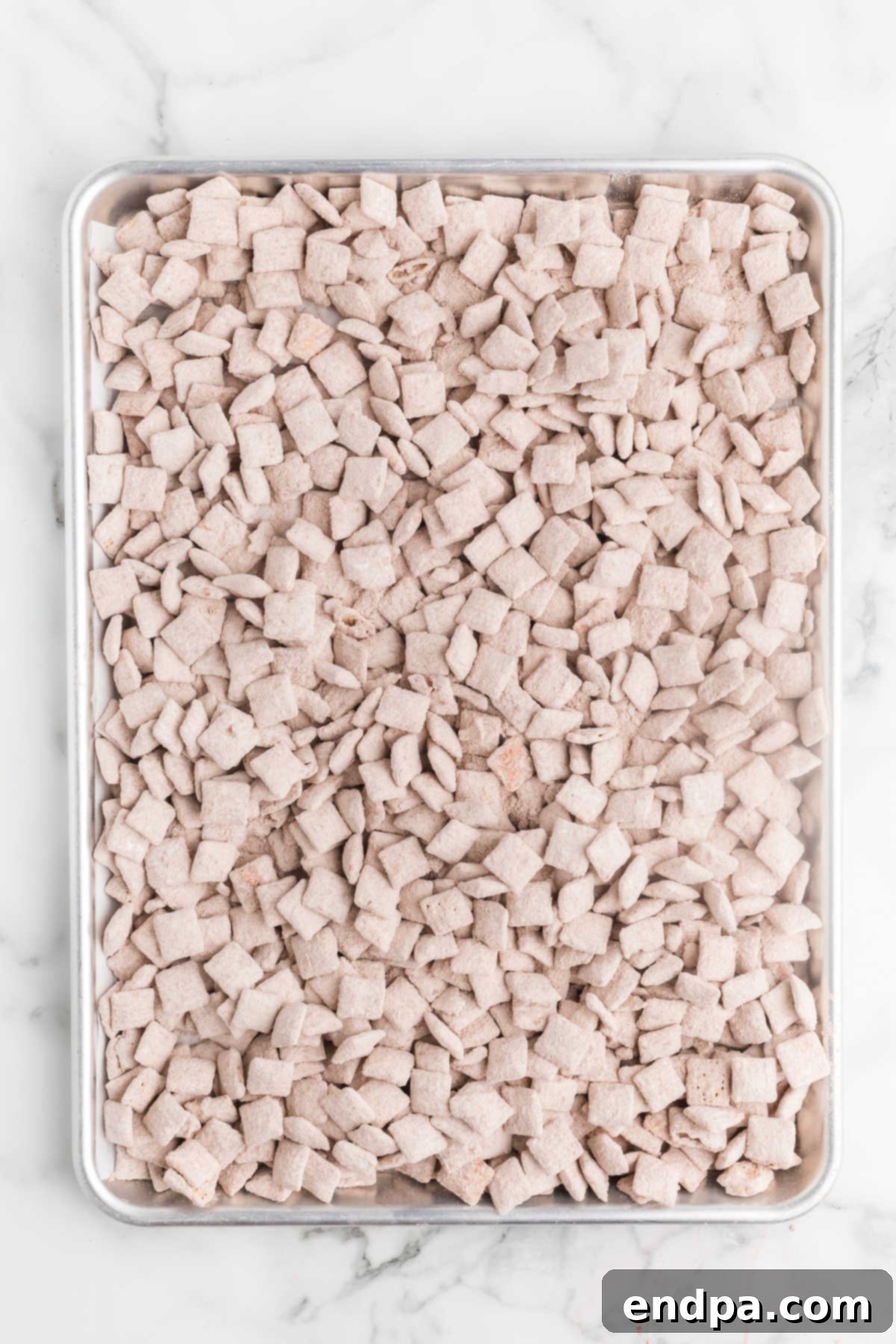 Coated Chex Mix spread on a baking sheet to cool and set after being shaken with red velvet cake mix and powdered sugar.