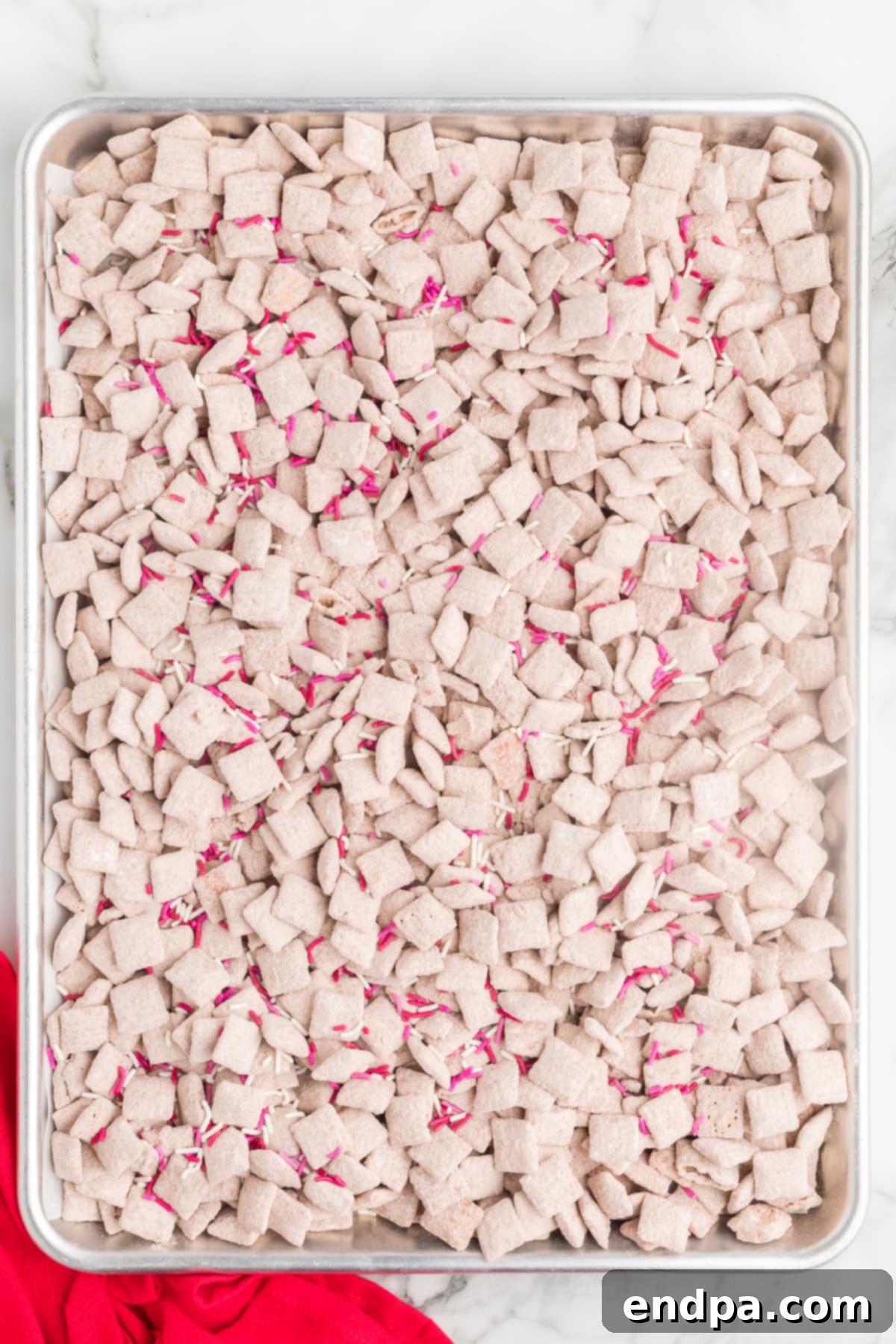 Finished Red Velvet Puppy Chow, cooled and topped with festive sprinkles on a baking sheet.