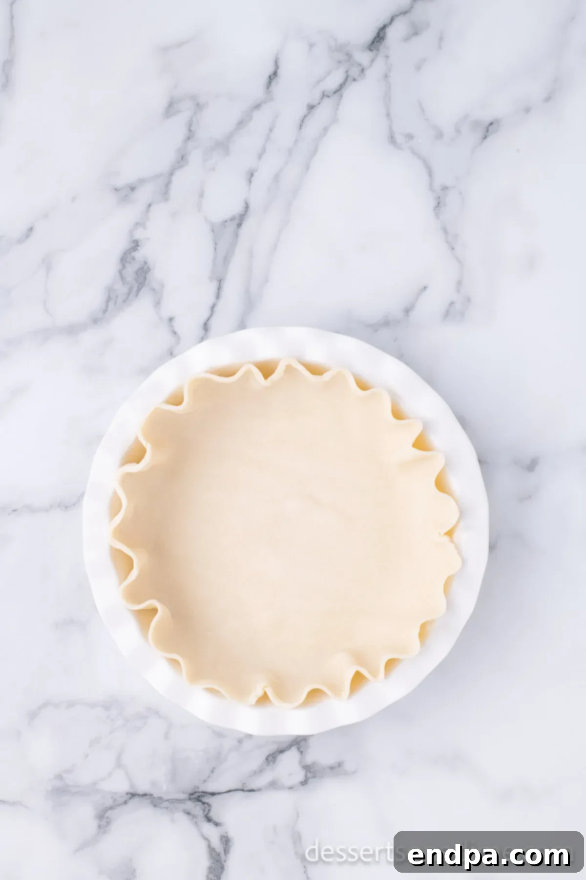 An unbaked pie crust neatly placed and crimped in a 9-inch ceramic pie plate, ready for the filling.