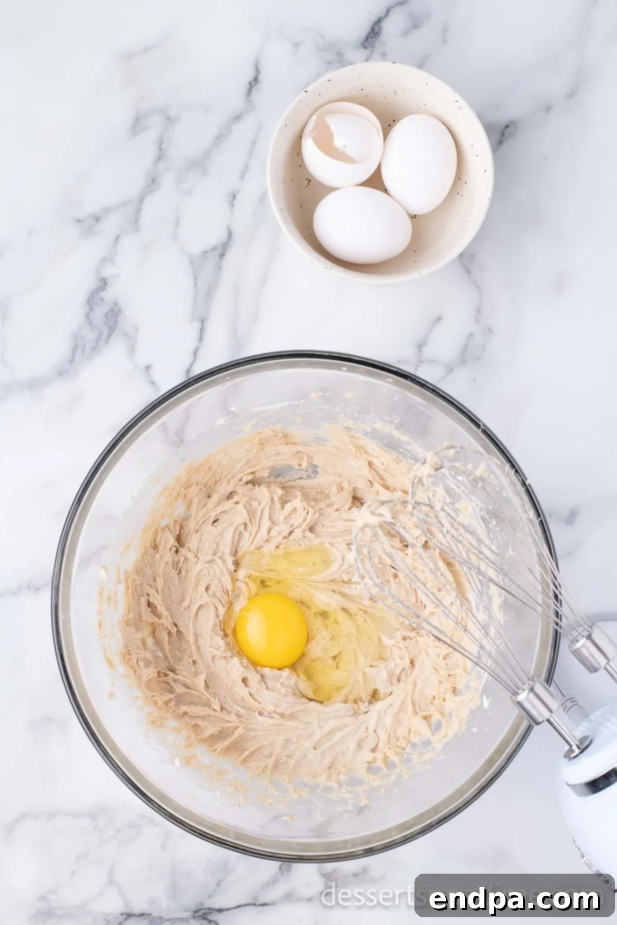 Beaten eggs are being incorporated into the cream cheese and brown sugar mixture in a mixing bowl.