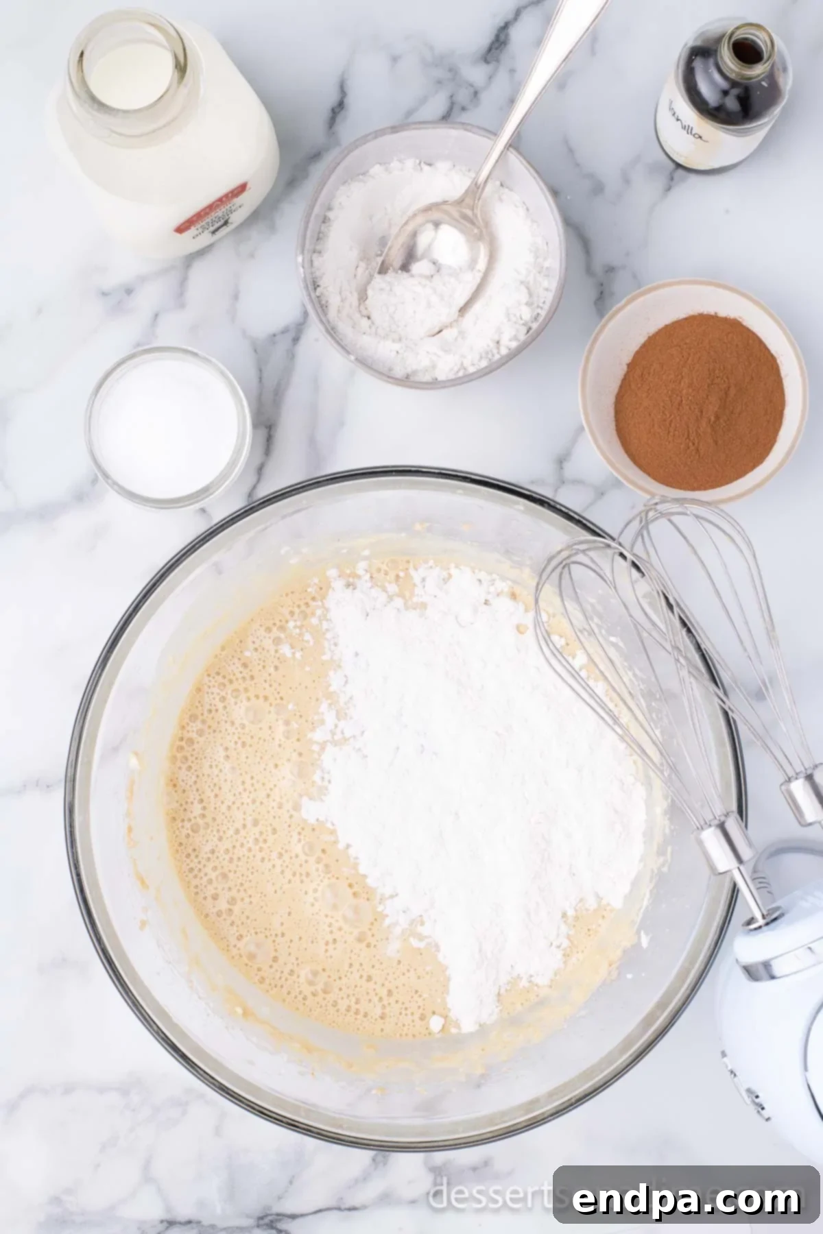 All the remaining dry ingredients, including flour, cinnamon, and salt, are being gradually added to the wet cream cheese and egg mixture in a bowl.