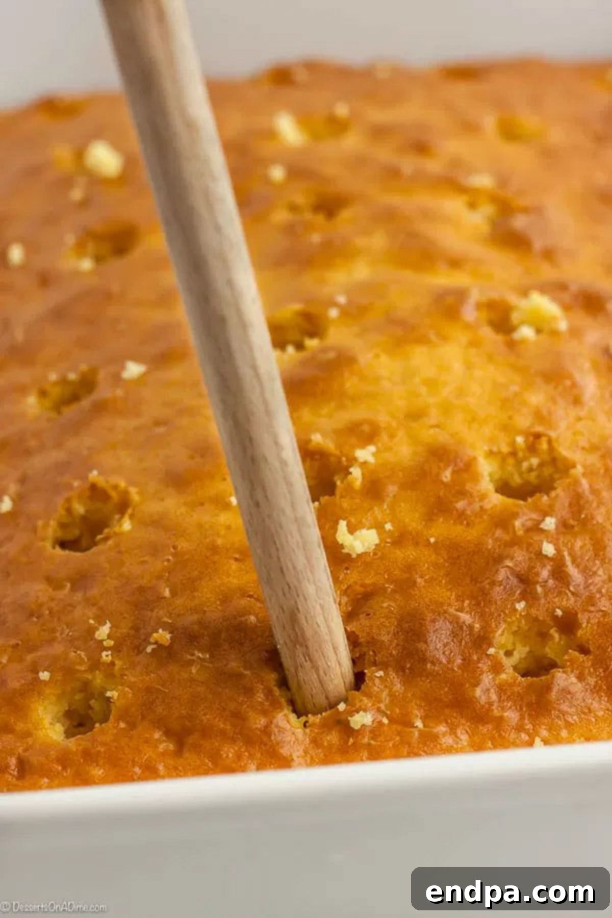 Banana Dream Pudding Cake 3 Holes being poked into the cake with the end of a wooden spoon