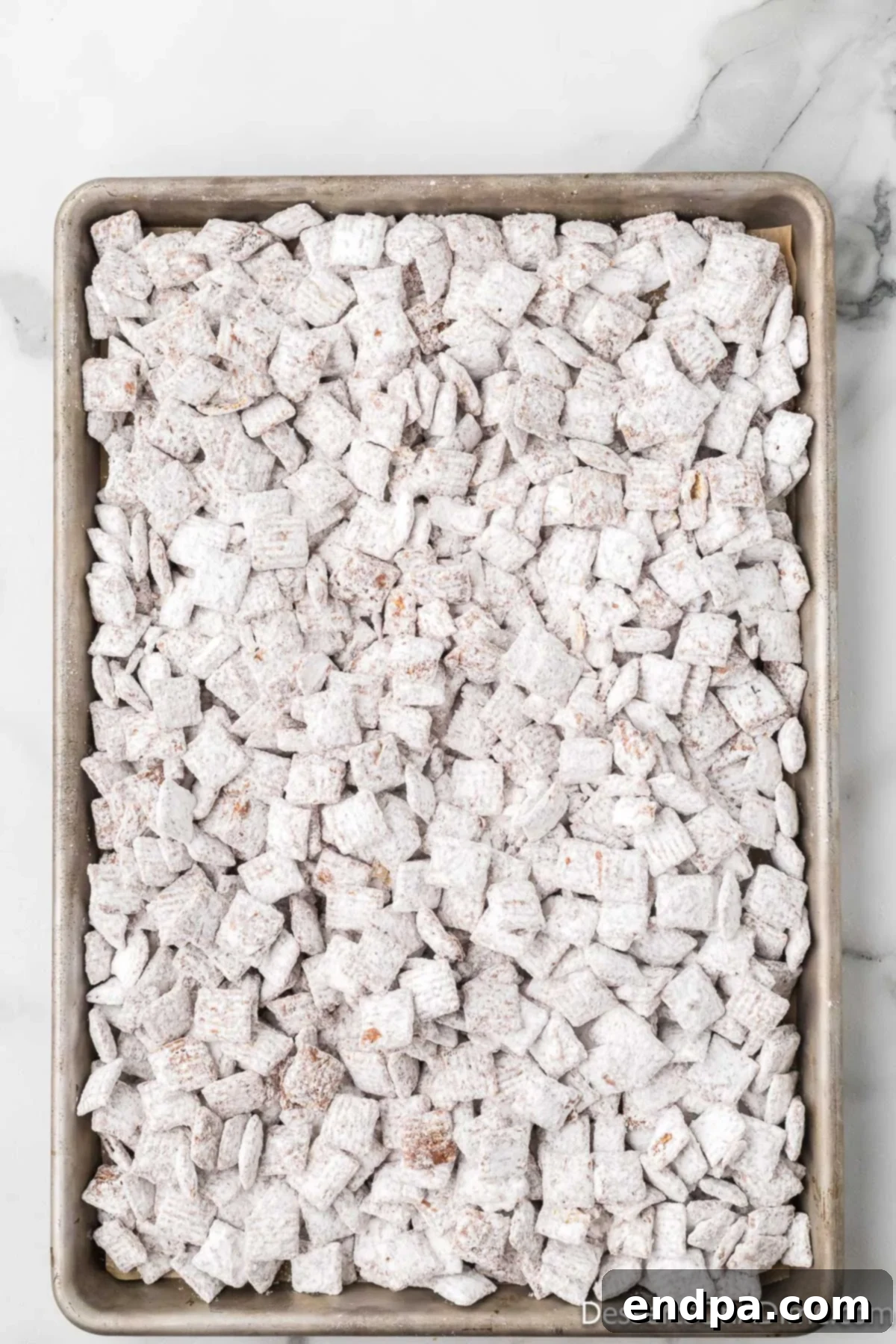 Powdered sugar-coated Chex cereal spread out on a baking sheet to cool.