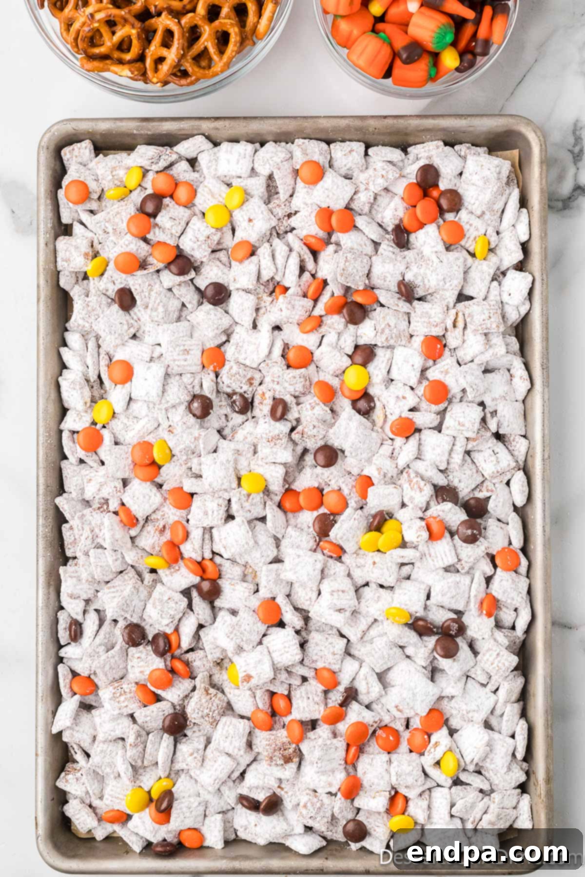 Reese's Pieces candies being added to the cooled Puppy Chow mixture.