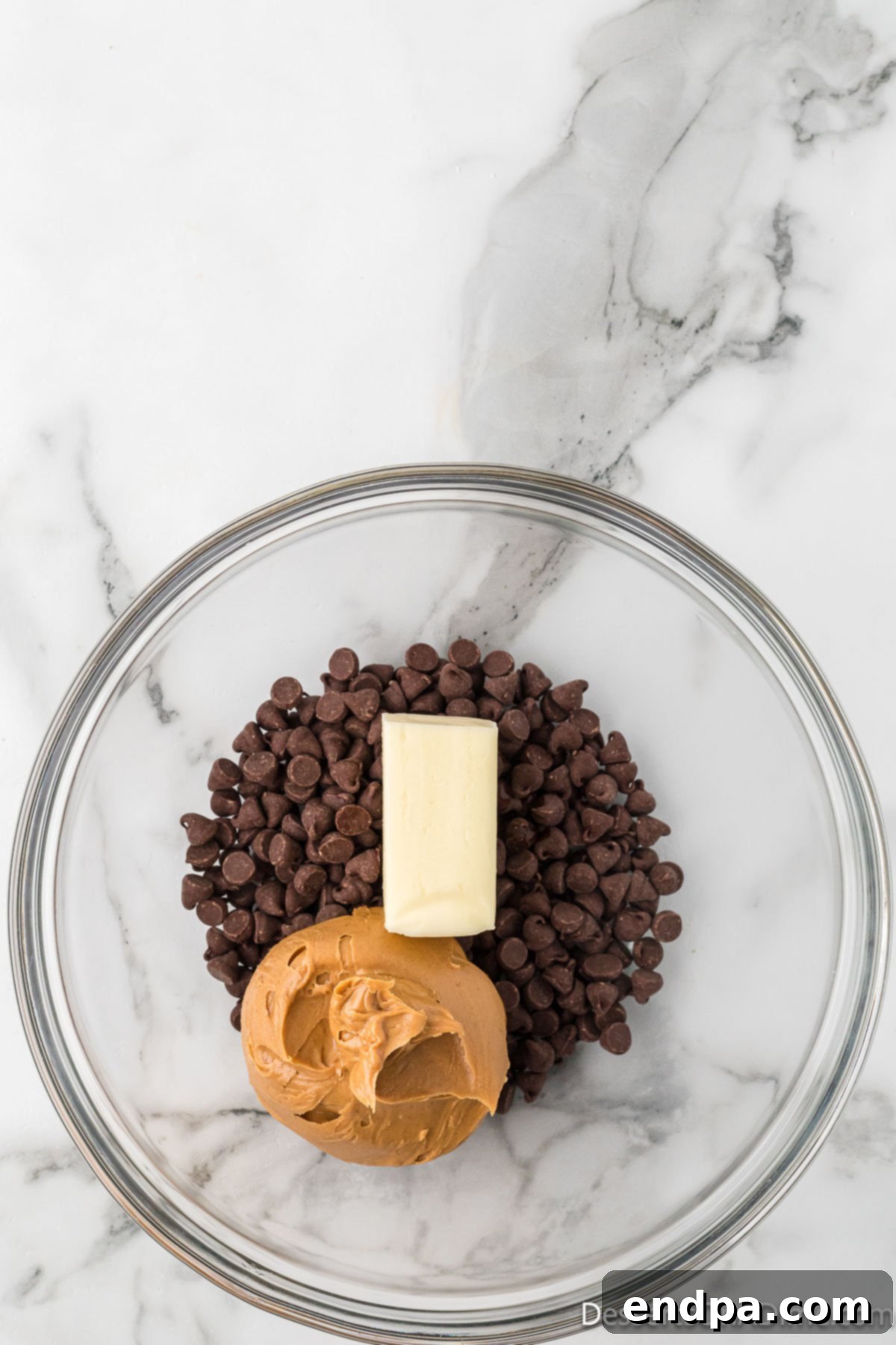 A mixing bowl containing chocolate chips, butter, peanut butter, and vanilla extract.