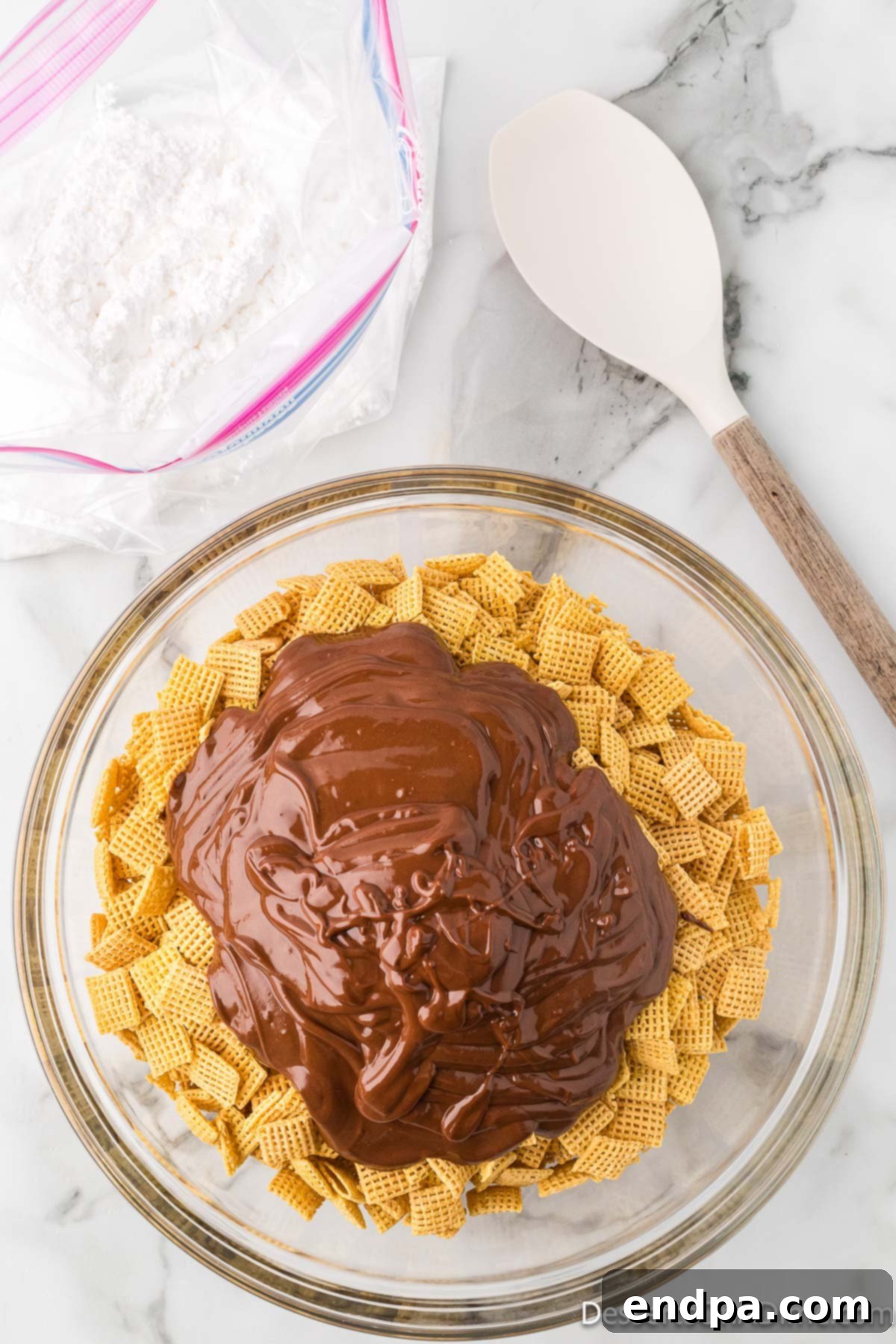 Melted chocolate mixture being poured evenly over Chex cereal in a bowl.