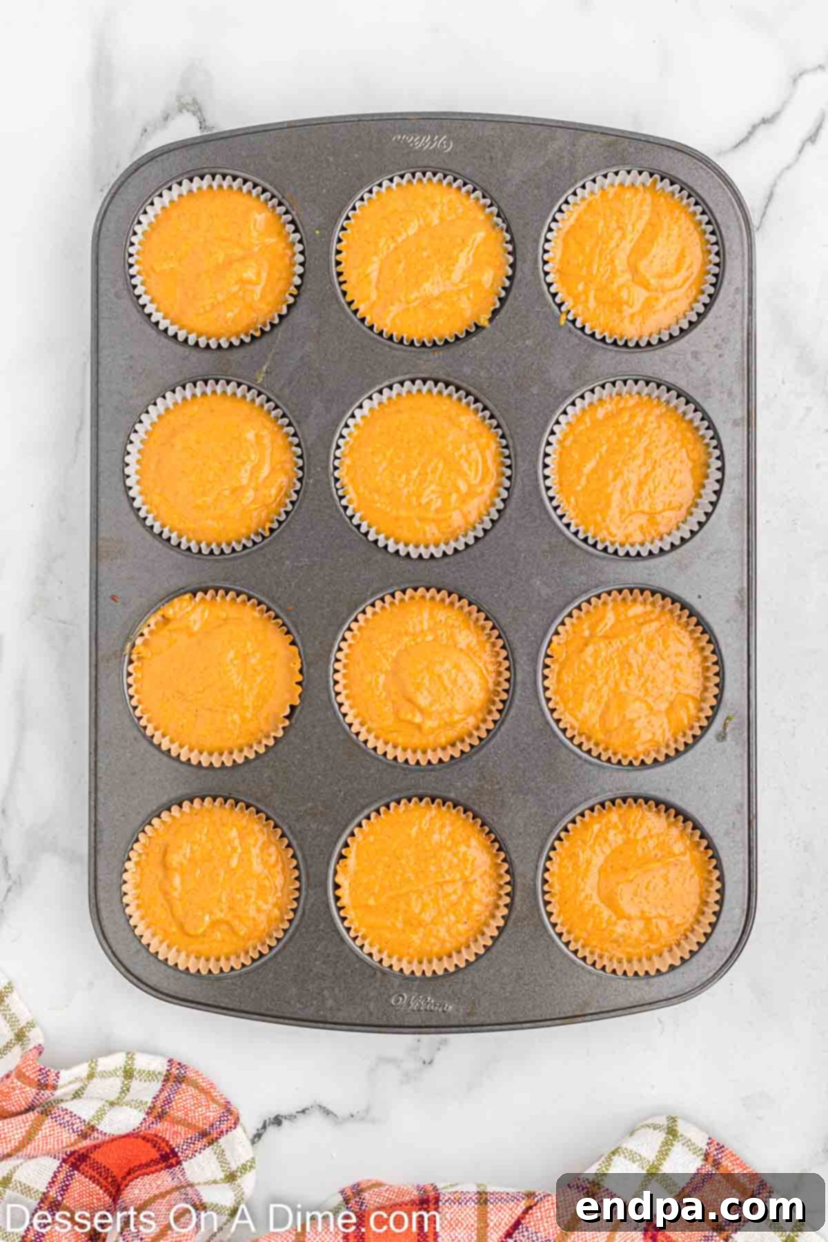 Placing the pumpkin cupcake batter into the muffin pan liners, filling each approximately half full.
