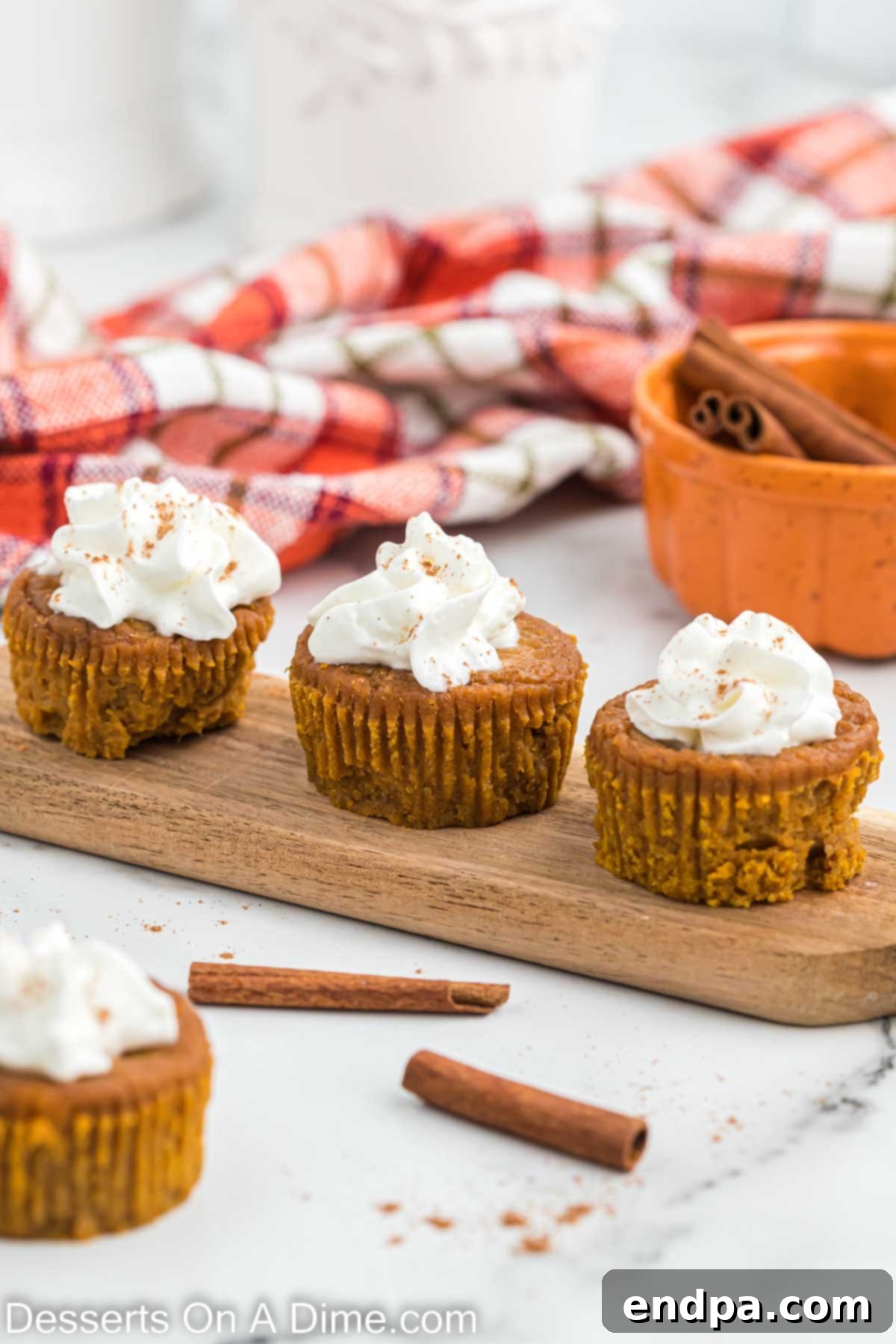 Close up image of pumpkin cupcakes topped with whipped cream and a sprinkle of cinnamon, arranged on a rustic wooden platter.