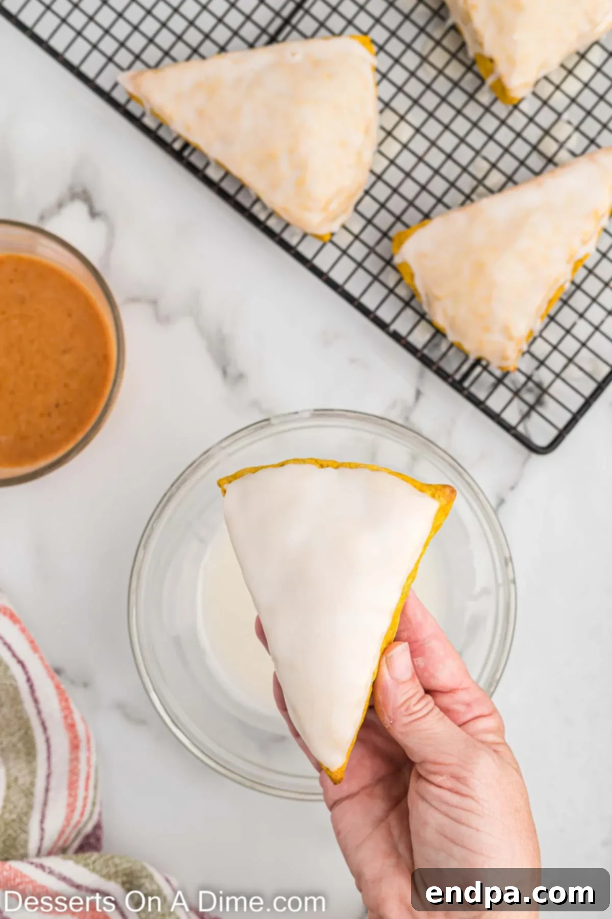Warm pumpkin scones being dipped upside down into a bowl of white glaze to coat the tops evenly.